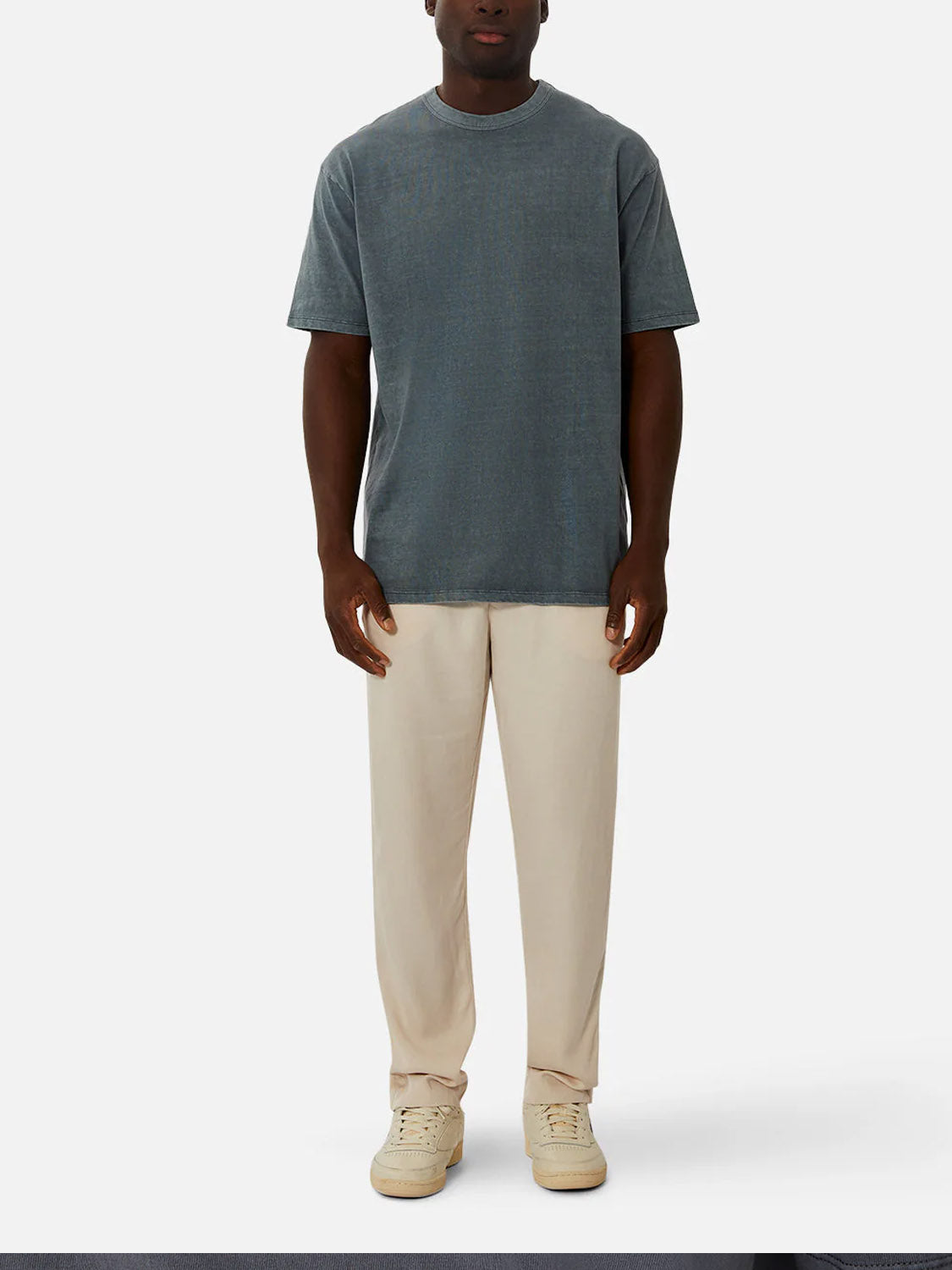 A man stands against a white background, wearing Industrie’s The Del Sur Tee in faded blue-grey. The relaxed fit crew neck t-shirt is made from 100% cotton, styled with beige pants and cream sneakers, his arms resting by his sides.