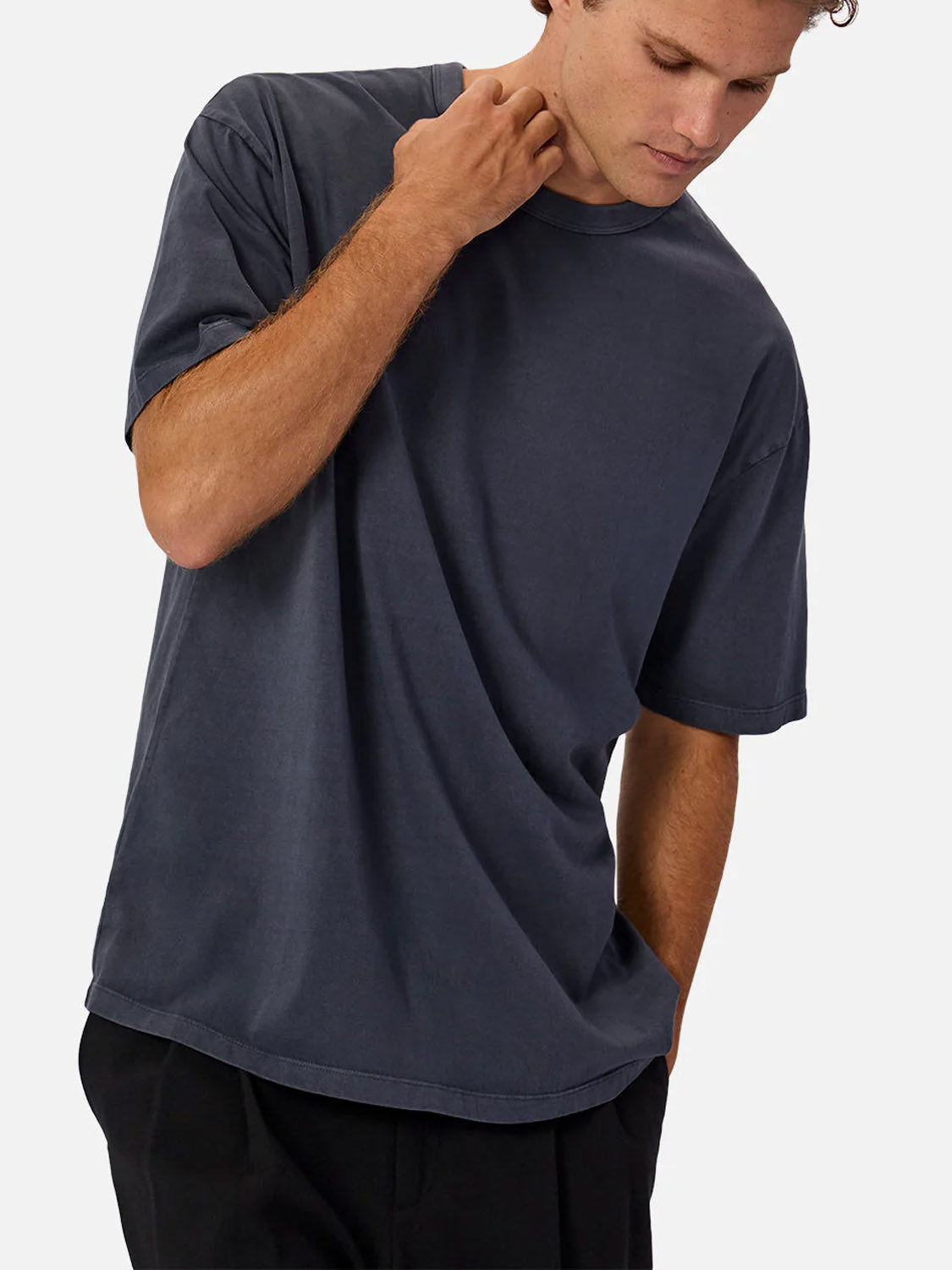 A person wears Industrie’s The Del Sur Tee, a relaxed-fit, short-sleeved dark gray 100% cotton crew neck t-shirt, with black pants, posing against a plain white background—one hand on their neck, the other in their pocket.