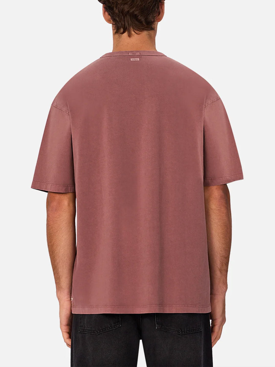 A person is shown from the back wearing Industrie’s The Del Sur Tee, a loose-fitting, short-sleeve, dusty rose 100% cotton crew neck t-shirt, paired with black jeans against a plain white background.