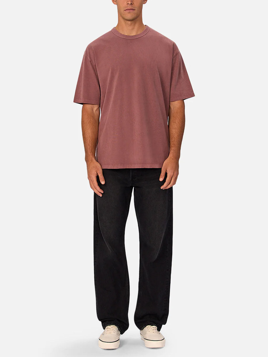 A man faces forward against a light background, wearing the Industrie Del Sur Tee in mauve—a relaxed fit, 100% cotton crew neck—paired with black baggy jeans and white sneakers.
