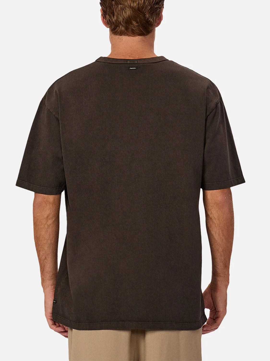 A person faces away from the camera in a relaxed-fit, short-sleeved dark brown Industrie The Del Sur Tee (100% cotton) and light beige pants, set against a plain white background.