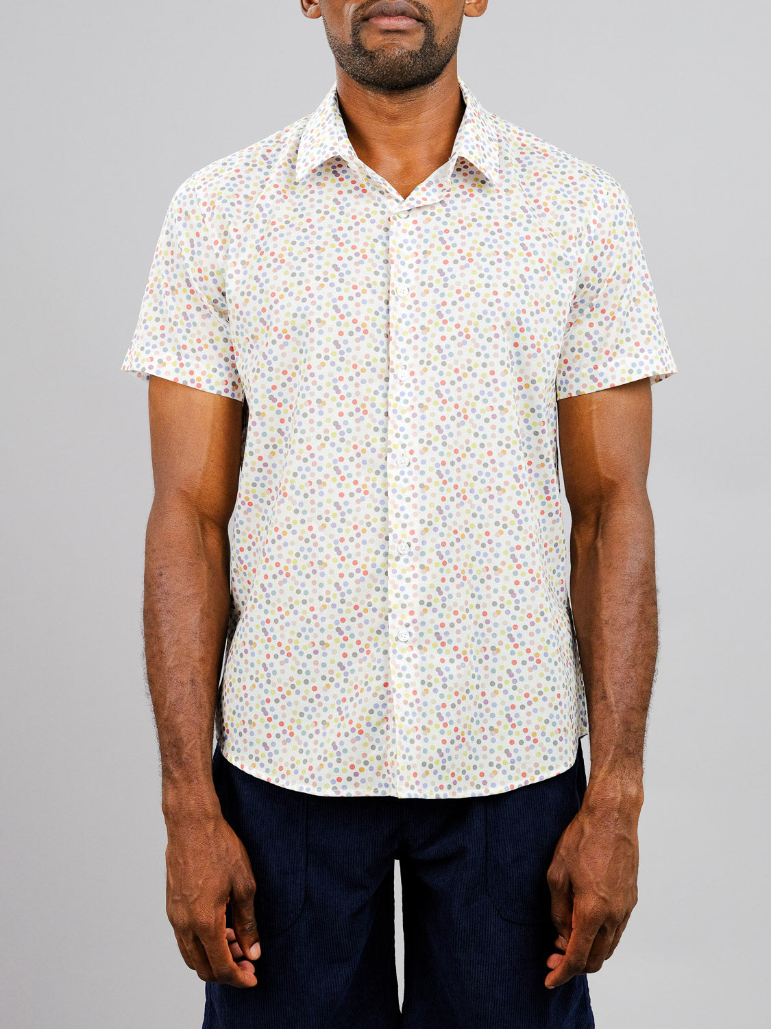 A man in the Disco Printed Cotton Shirt by ID Menswear, featuring a lightweight, short-sleeve cotton build with a vibrant print, paired with dark pants and standing against a plain light gray background.