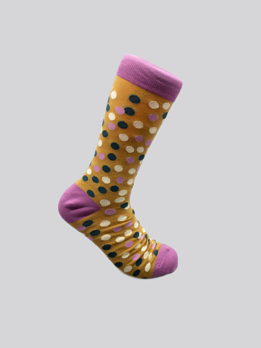 The Disco Graphic Sock by ID Menswear is a yellow, high-quality combed cotton sock with black, white, and pink polka dots and solid pink toe, heel, and cuff, shown on a gray background.