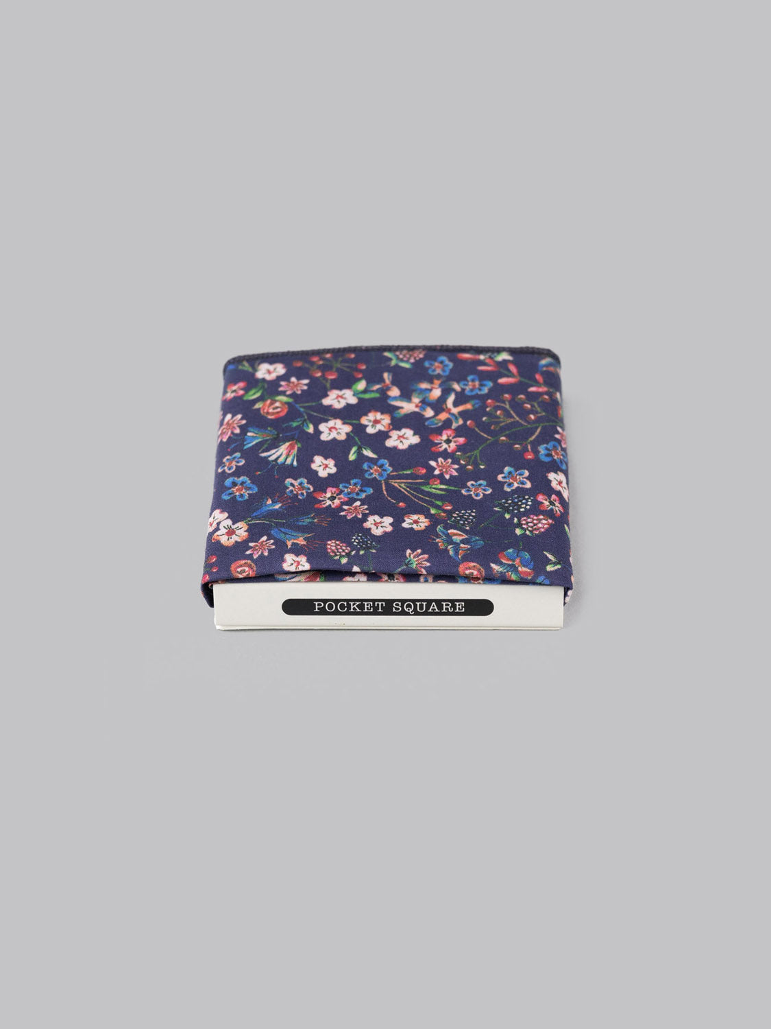 A folded Liberty™ Donna Pocket Square by ID Menswear, crafted from Tana Lawn cotton with a dark blue floral pattern, rests partially over a POCKET SQUARES box on a plain light gray background.