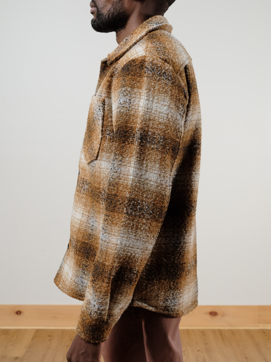 A man stands in profile wearing the !SOLID Dronen Plaid Shirt Jacket in brown, white, and beige with a chest pocket. He is against a plain light background with a wooden floor visible at the bottom.
