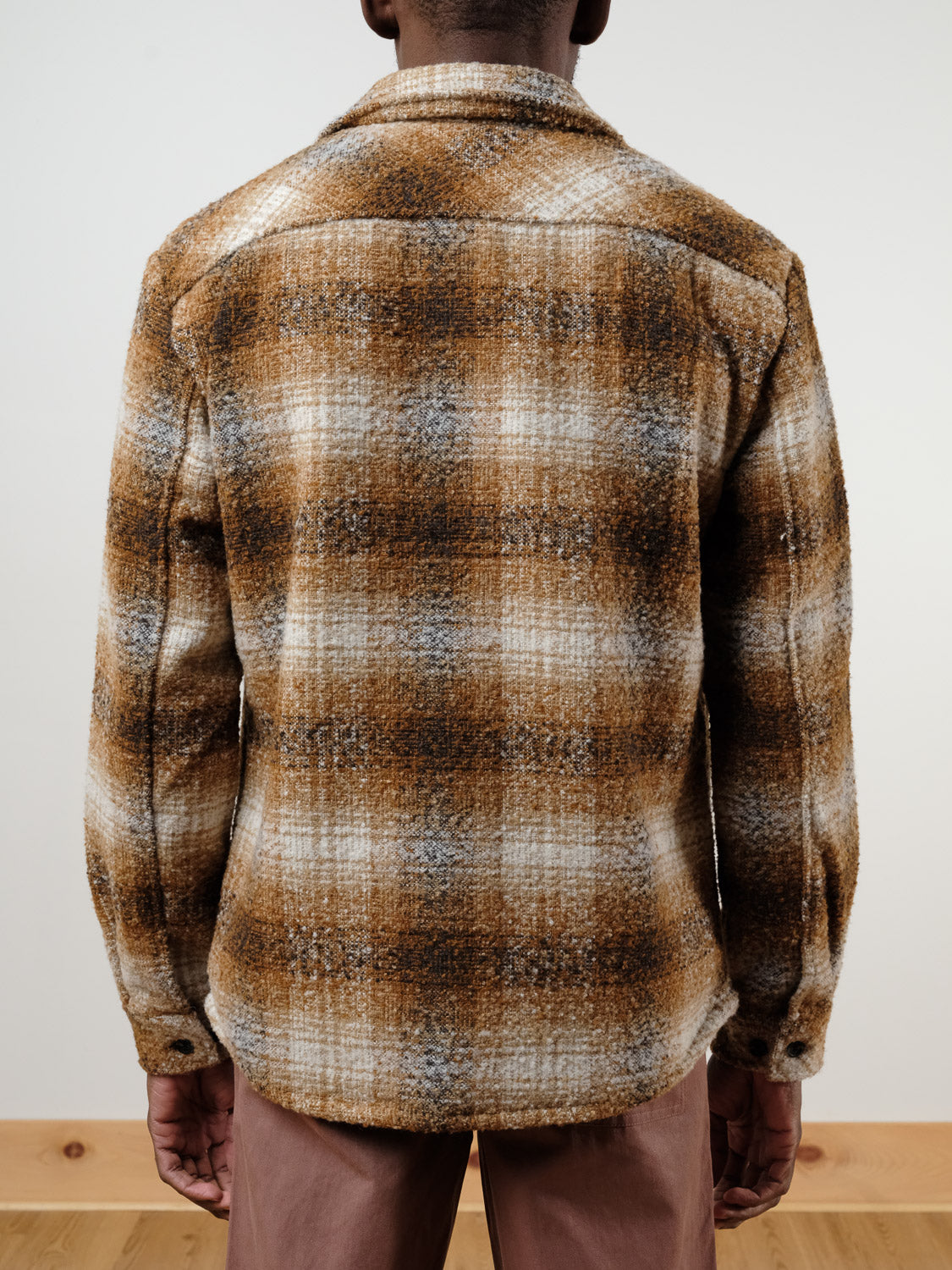 A person faces away from the camera, wearing the !SOLID Dronen Plaid Shirt Jacket in brown, tan, white, and gray plaid with a relaxed fit and textured look. It's paired with light brown pants against a plain, light background.