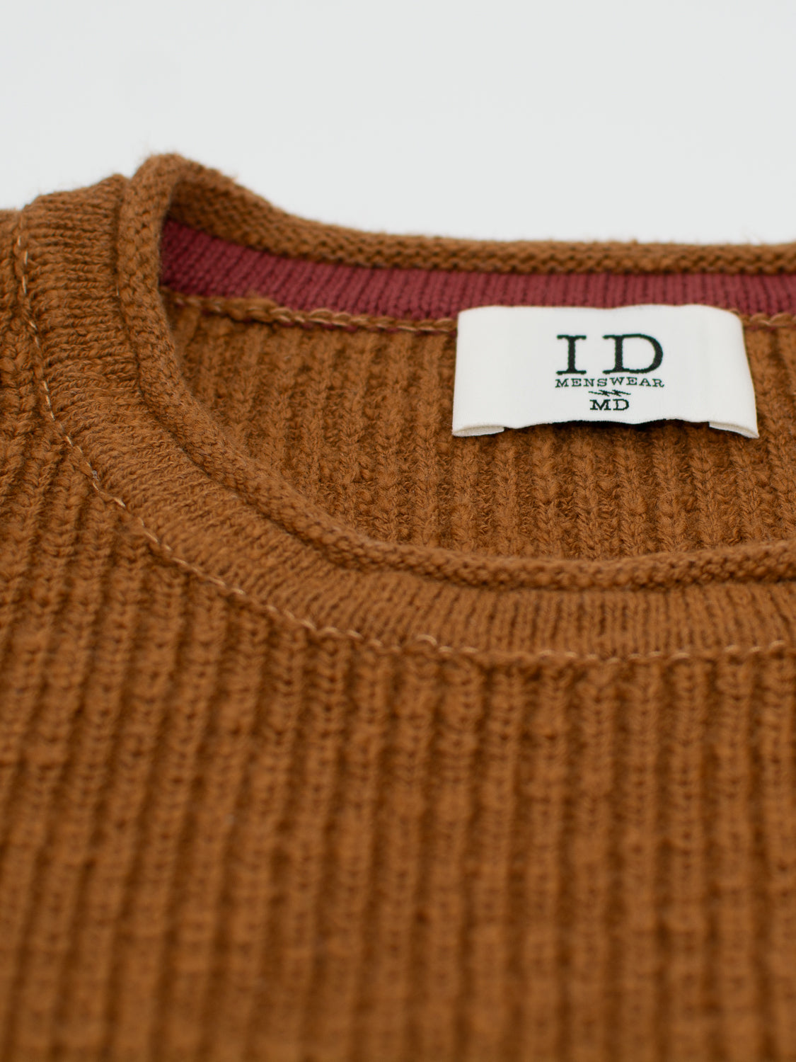 Close-up of a brown ribbed Dublin Slub Cotton Rolled Neck Sweater by ID Menswear, featuring a visible label at the neck. Crafted for cooler weather, it boasts a round neckline with subtle red trim inside, adding warmth and style.
