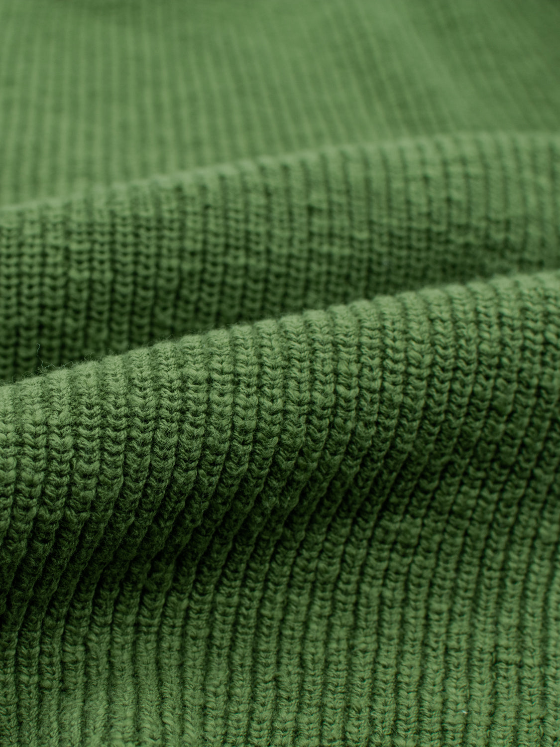 Close-up of the green Dublin Slub Cotton Rolled Neck Sweater by ID Menswear, showcasing its ribbed texture with vertical lines. Ideal for cooler weather, the softly folded fabric highlights its woven structure and rich color reminiscent of a classic Dublin sweater.