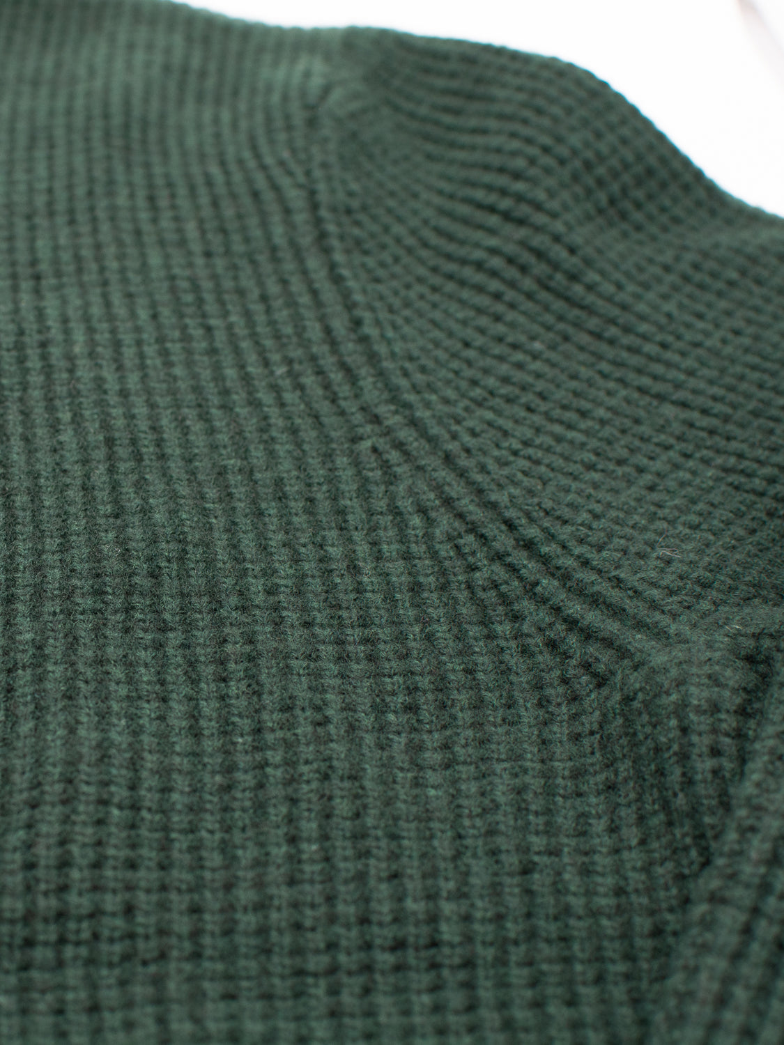 Close-up of the Dundee Waffle Knit Merino Cardigan by ID Menswear in dark green, highlighting its textured, grid-like waffle pattern and detailed stitching along a curved seam.