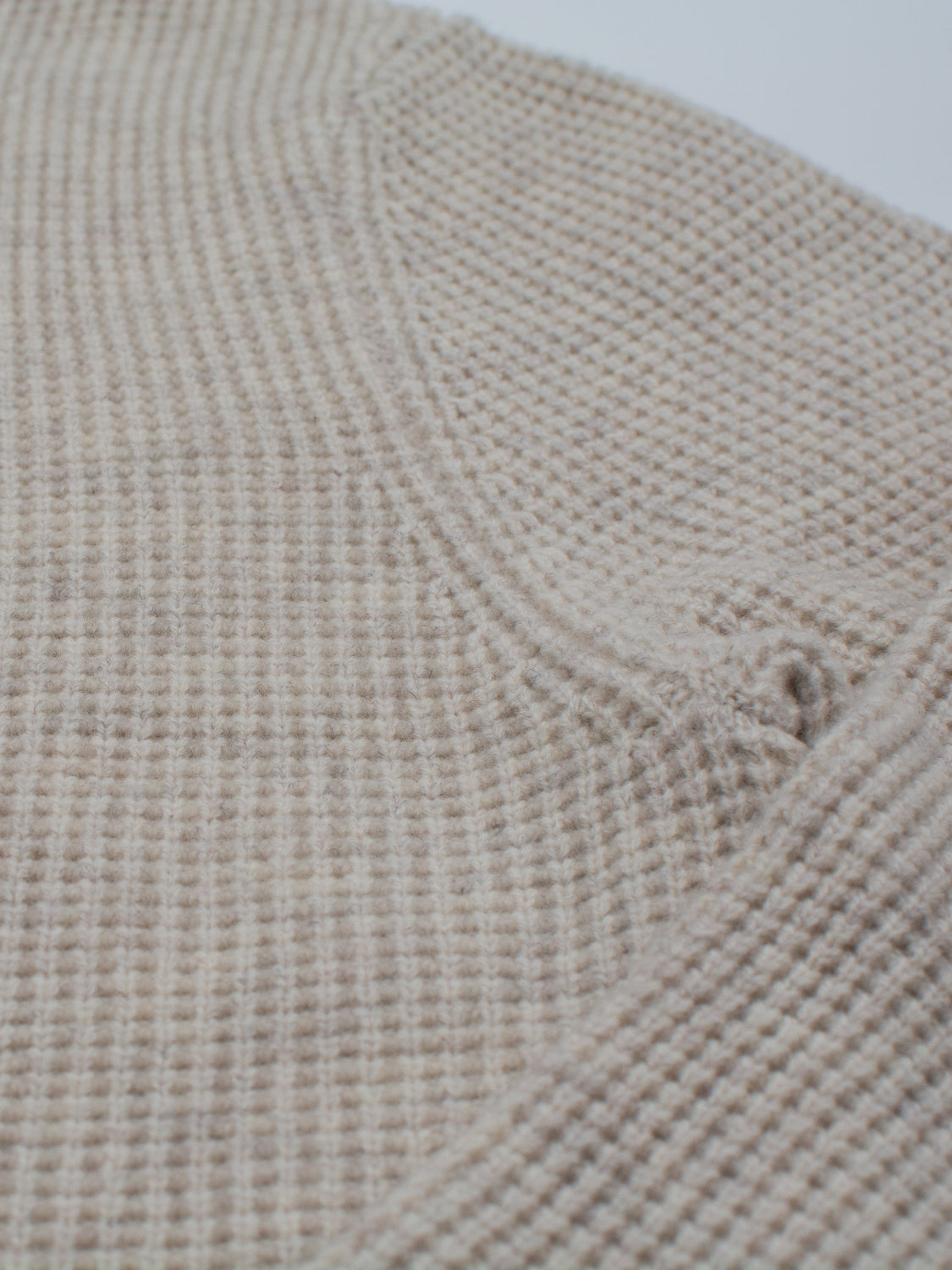 Close-up of beige waffle-knit fabric shows textured pattern and stitching along a seam—ideal for the Dundee Waffle Knit Merino Cardigan by ID Menswear.