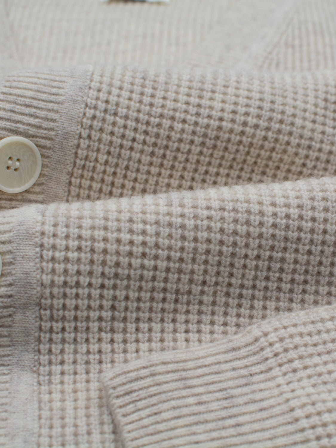 Close-up of the Dundee Waffle Knit Merino Cardigan by ID Menswear, featuring a soft beige texture, two cream buttons, and ribbed cuffs. This men's cardigan offers a timeless, cozy style ideal for layering.