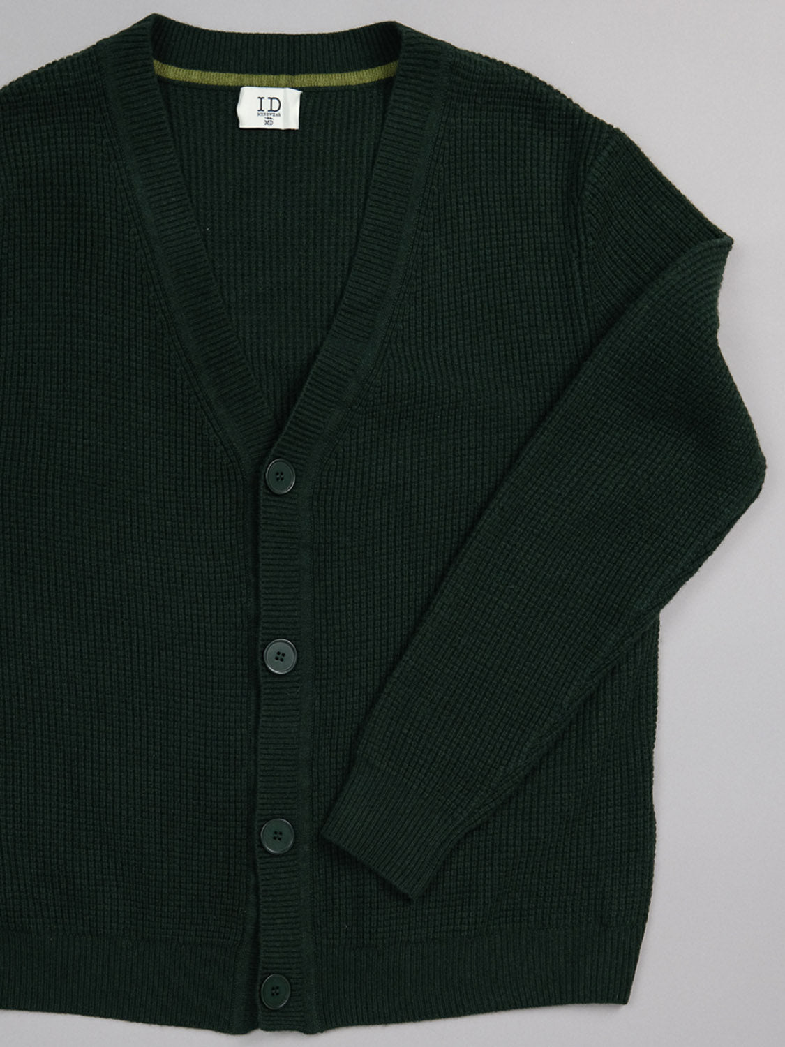 The Dundee Waffle Knit Merino Cardigan by ID Menswear is a dark green, long-sleeve men’s V-neck cardigan featuring a textured waffle knit, shown laid flat on a light gray surface.