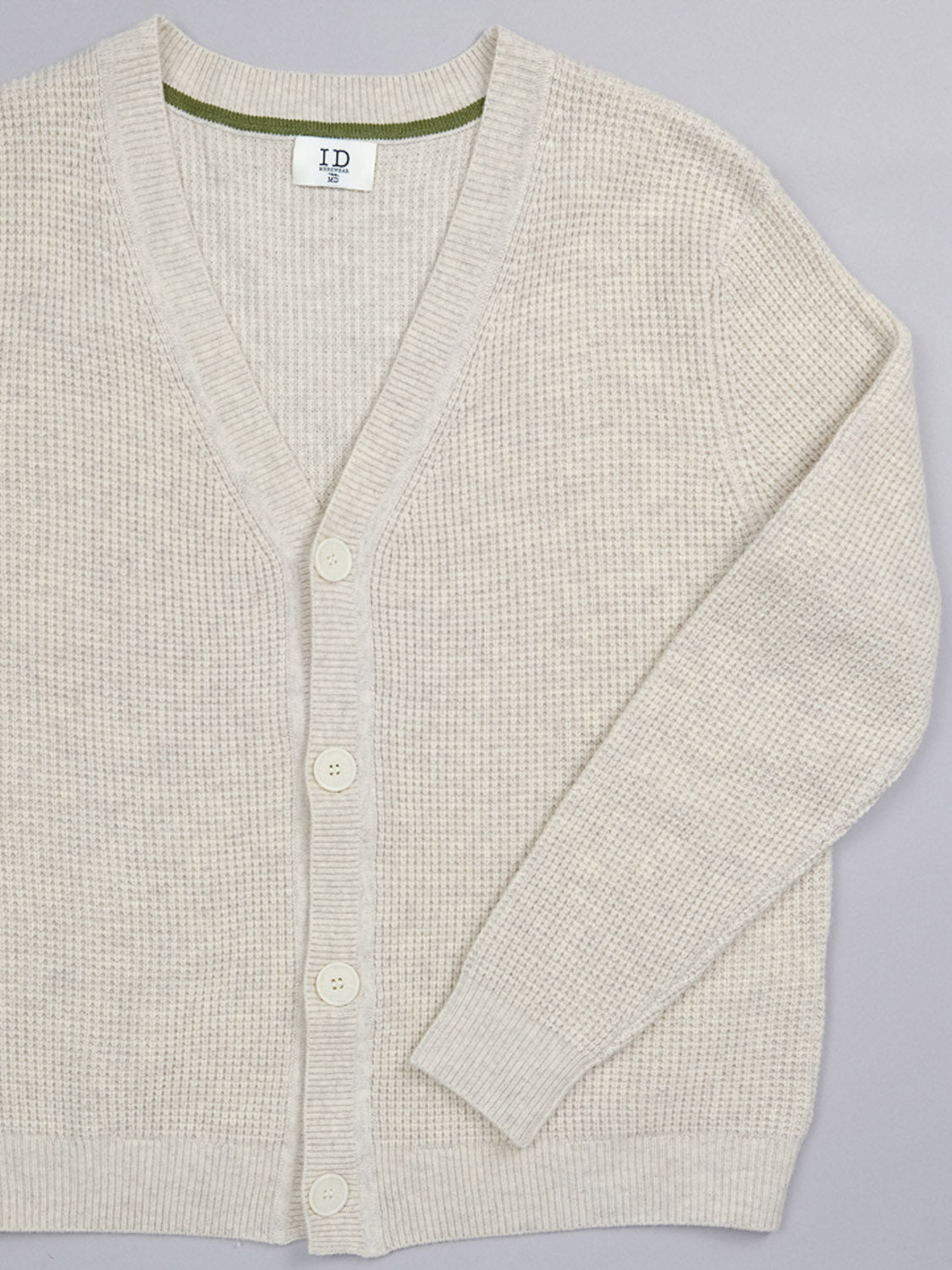 The Dundee Waffle Knit Merino Cardigan by ID Menswear, in cream with long sleeves, a V-neck, four white buttons, and a subtle textured pattern, is laid flat on a light background.