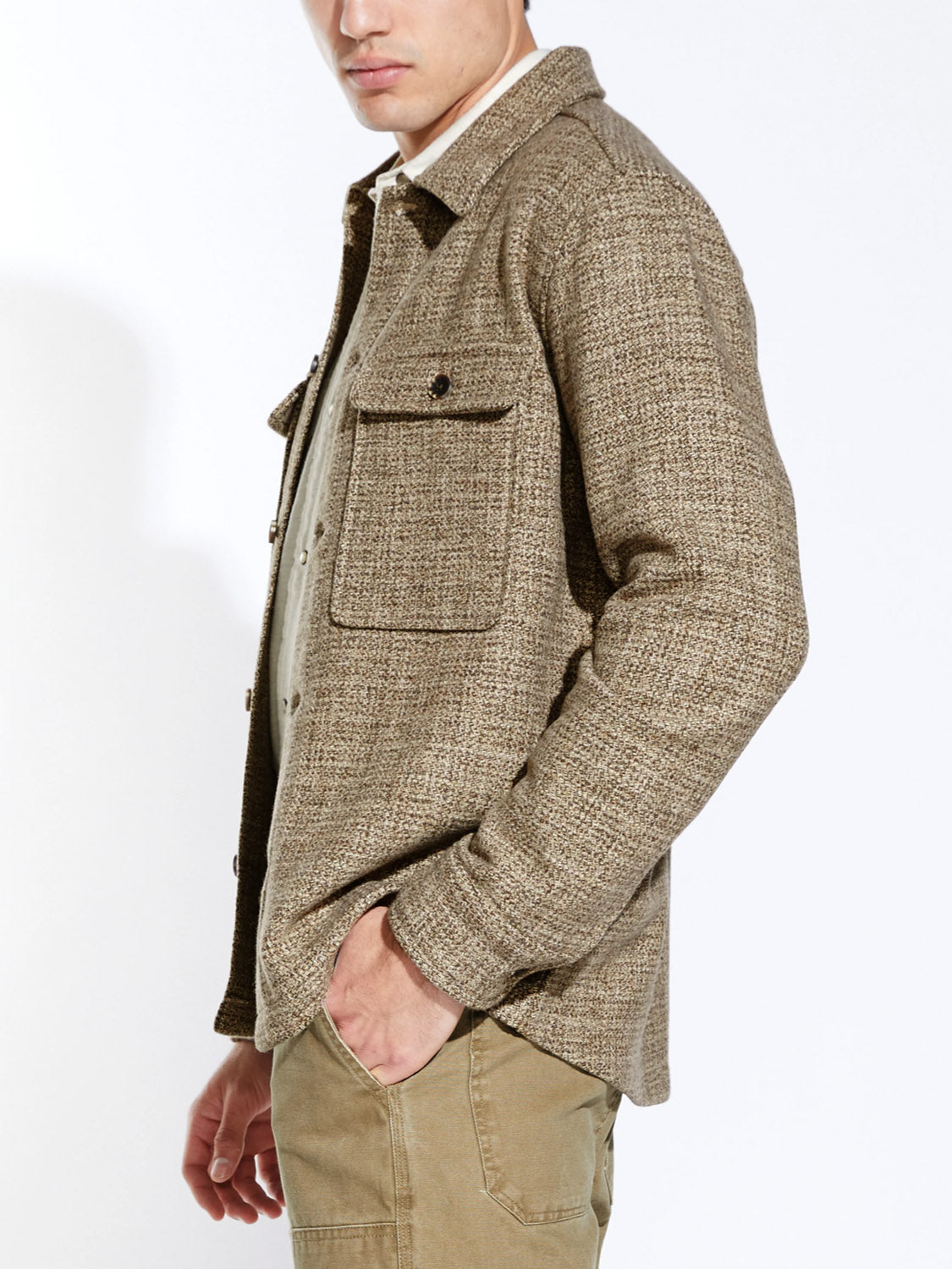 A man models the Civil Society Durbin Relaxed Fit Shirt Jacket in brown marled twill, featuring large front pockets, paired with tan pants. He stands sideways with a hand in his pocket against a plain white background.