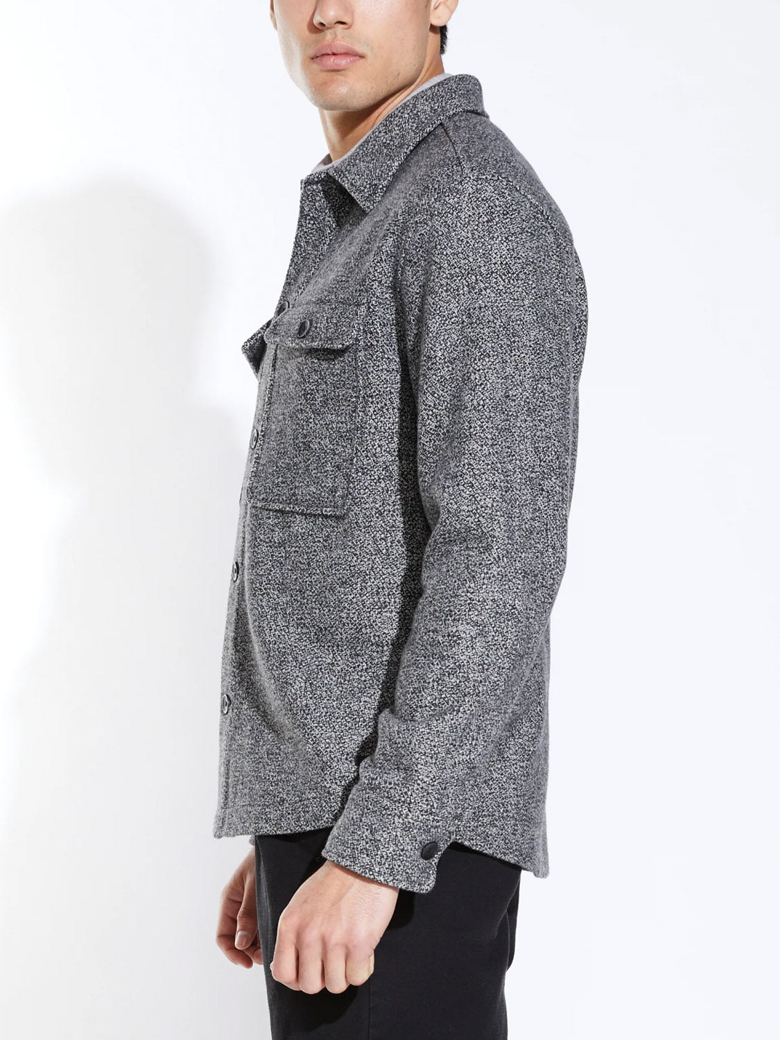 A man stands sideways against a white background, wearing black pants and the Civil Society Durbin Relaxed Fit Shirt Jacket, which features a marled twill fabric and chest pocket.