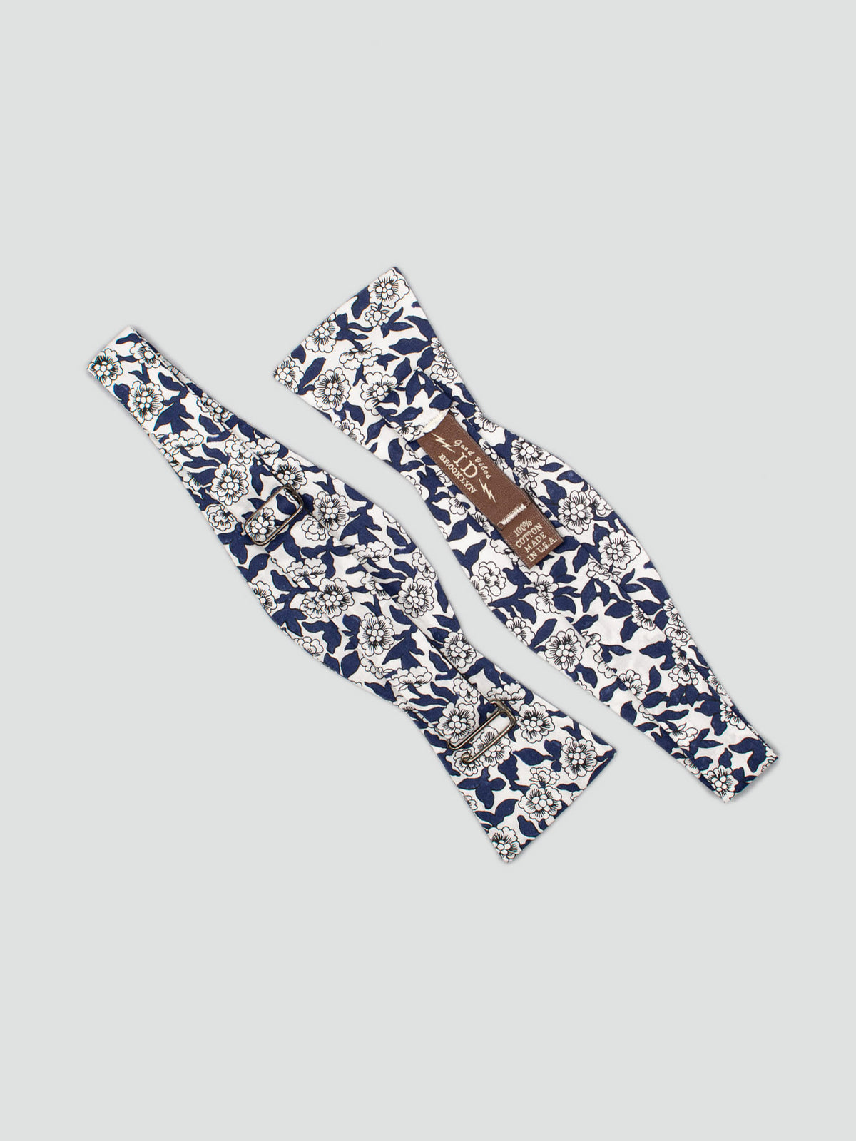 Two Liberty of London Tana Lawn™ Dynasty Bow Ties by ID Menswear, featuring blue and white floral patterns, are displayed flat on a light grey background with the adjustable clasp and label visible.
