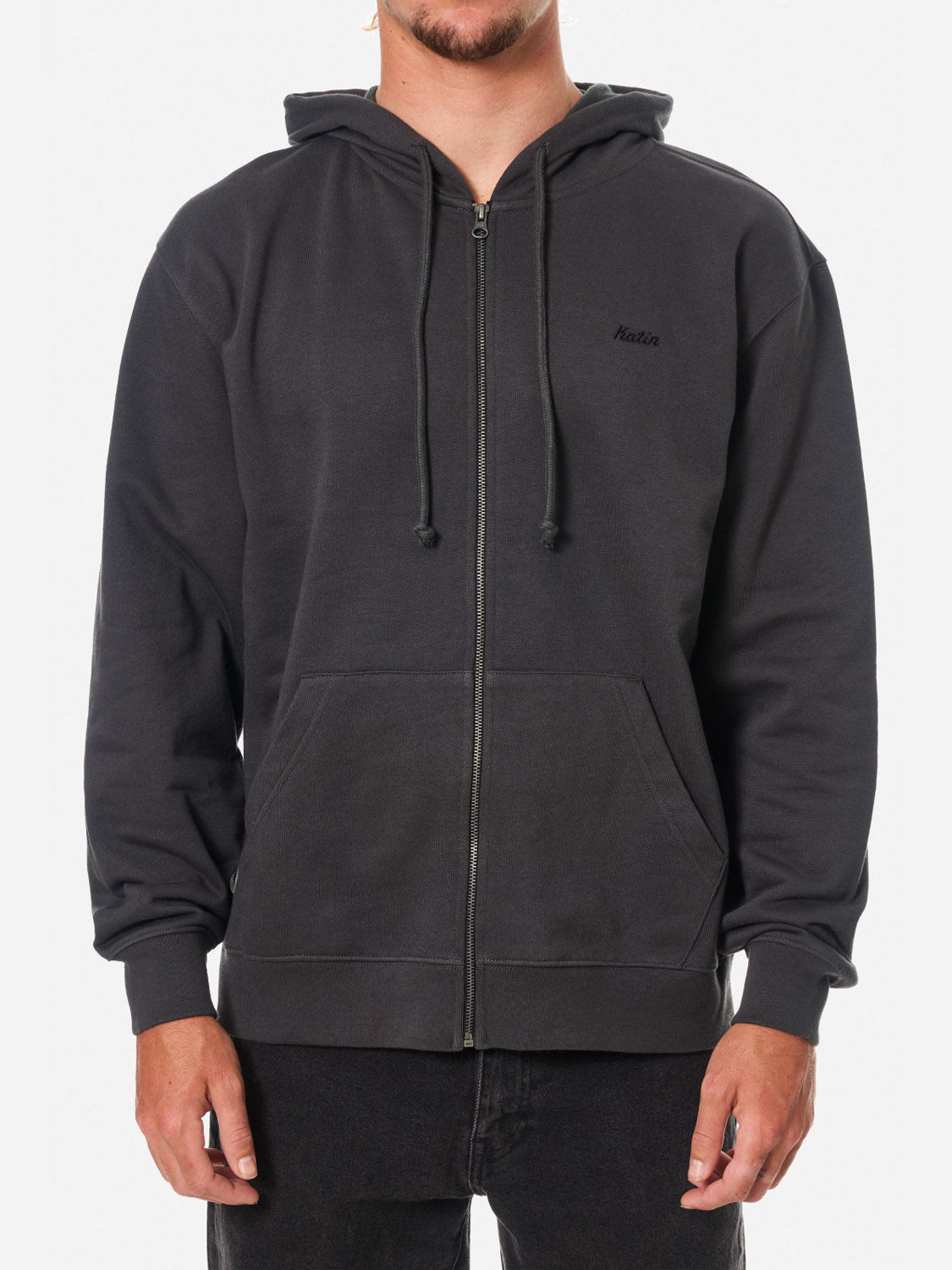 A person wears the Katin Embroidered Full Zip Hoodie with a hood, drawstrings, and front pockets, paired with black pants against a plain white background.