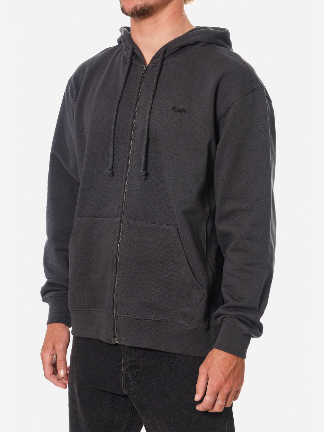 A person wears the Katin Embroidered Full Zip Hoodie in black with a hood and drawstrings, paired with black pants, standing against a plain white background.