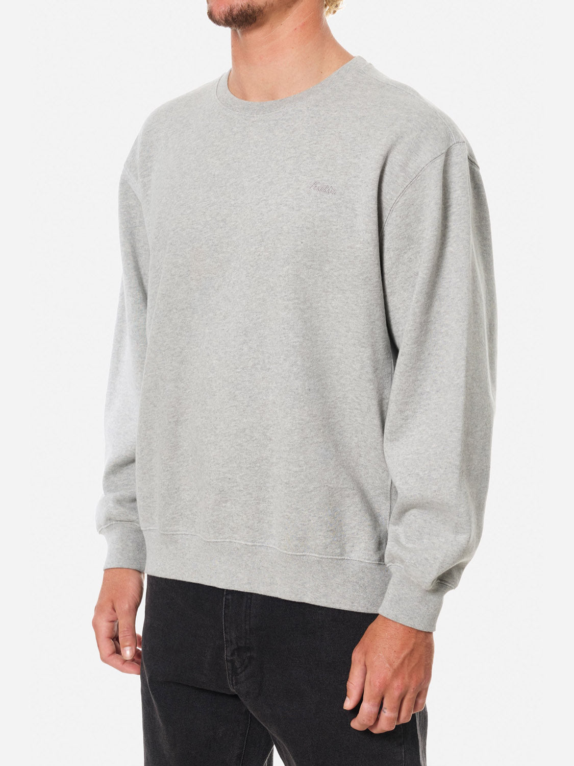 A man models the Katin Embroidered Crewneck in light gray with black jeans against a white background. His head is partially cropped out of the frame, and his arms hang relaxed at his sides.