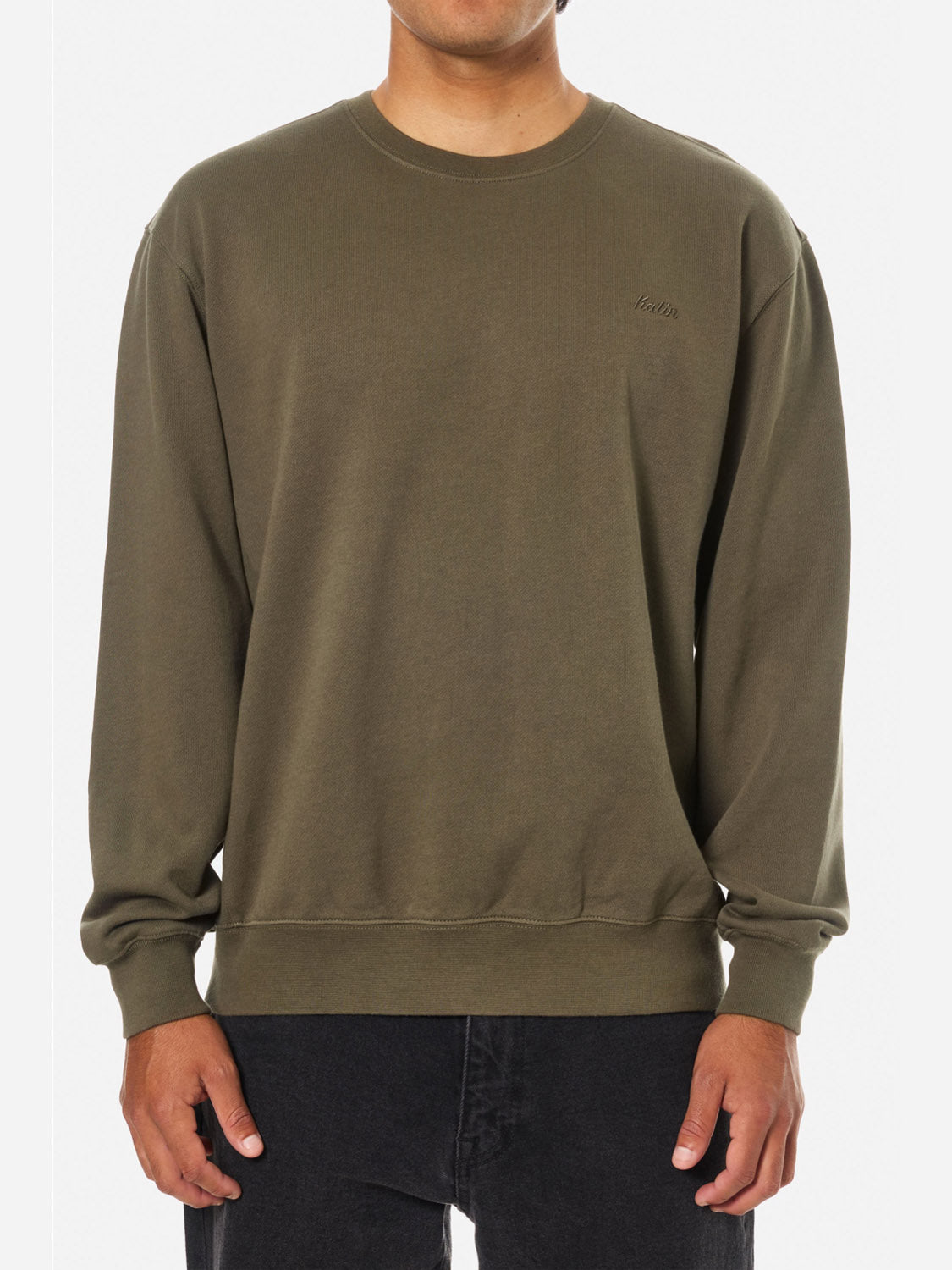 A person wears the Katin Embroidered Crewneck in olive green—featuring subtle left-chest embroidery and soft fleece—paired with black pants, standing against a plain white background.