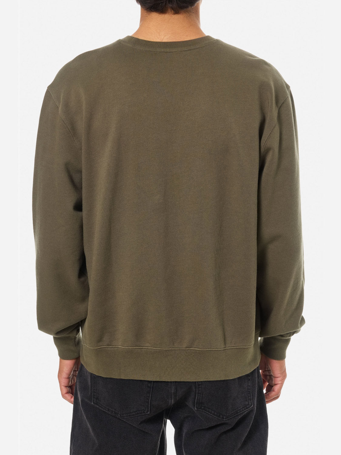 A person stands with their back to the camera against a plain white background, wearing the Katin Embroidered Crewneck in olive green and black jeans.
