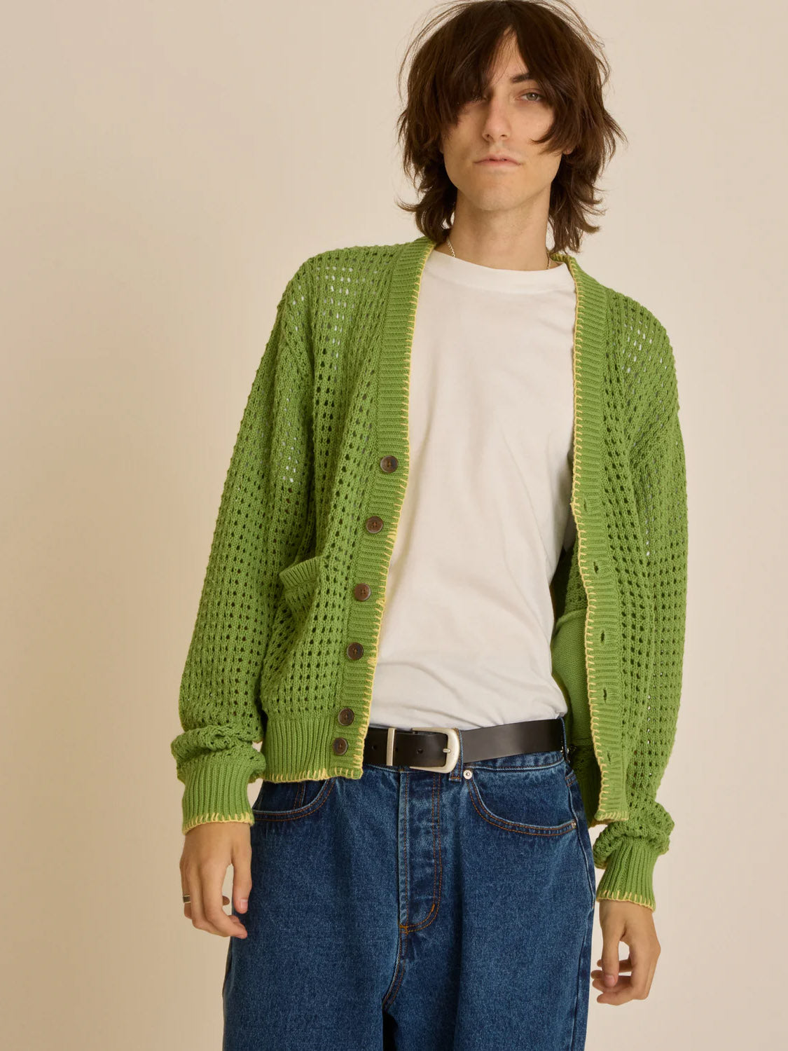 A person with long hair is wearing the Obey Ethan Cardigan over a white t-shirt and blue jeans, standing against a plain background with a neutral expression.