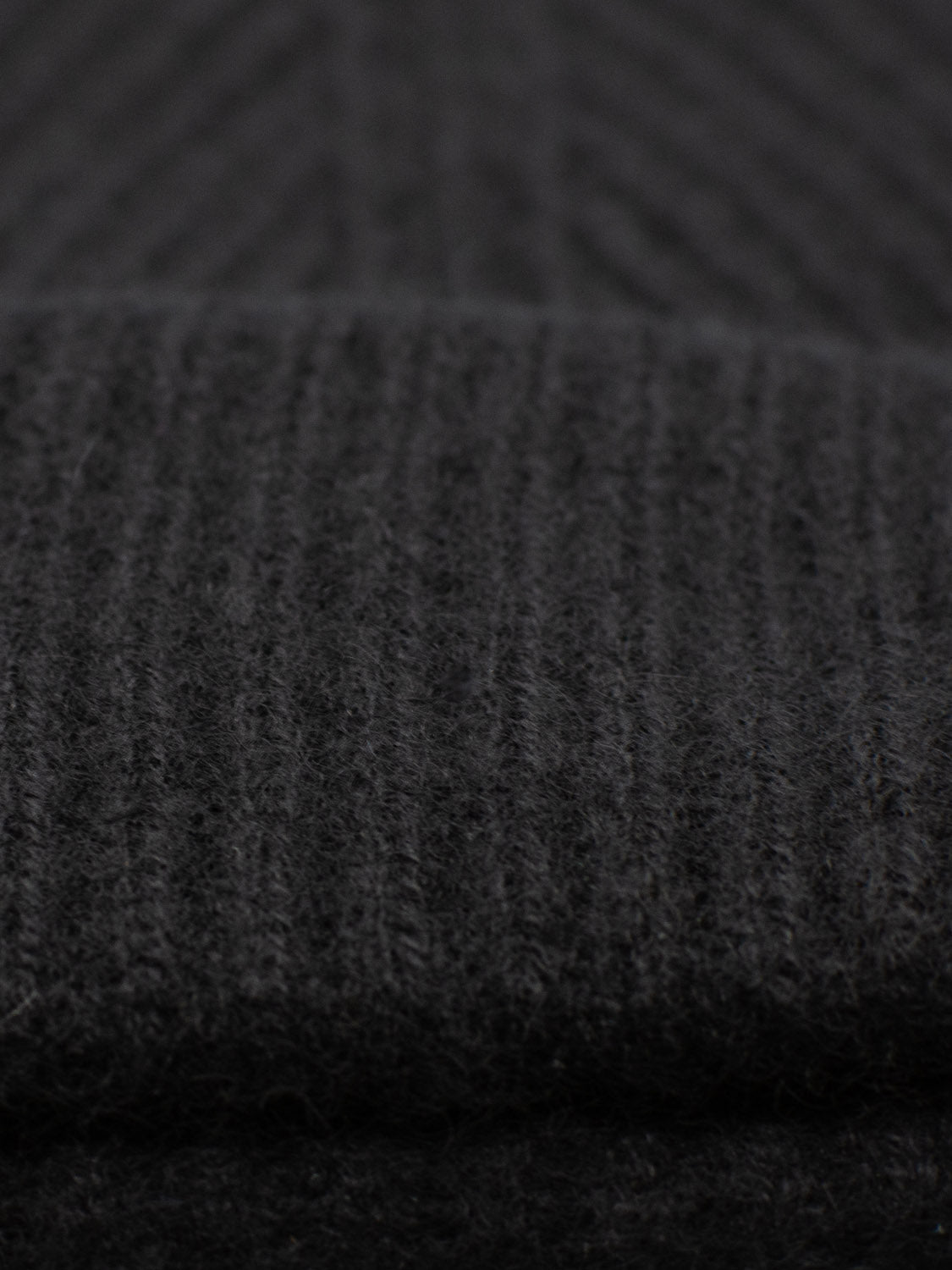 Close-up of the Everest Cashmere Beanie by ID Menswear features dark gray ribbed knit with soft, fuzzy fibers. Vertical lines and precise stitching highlight its versatile style and premium cashmere texture.