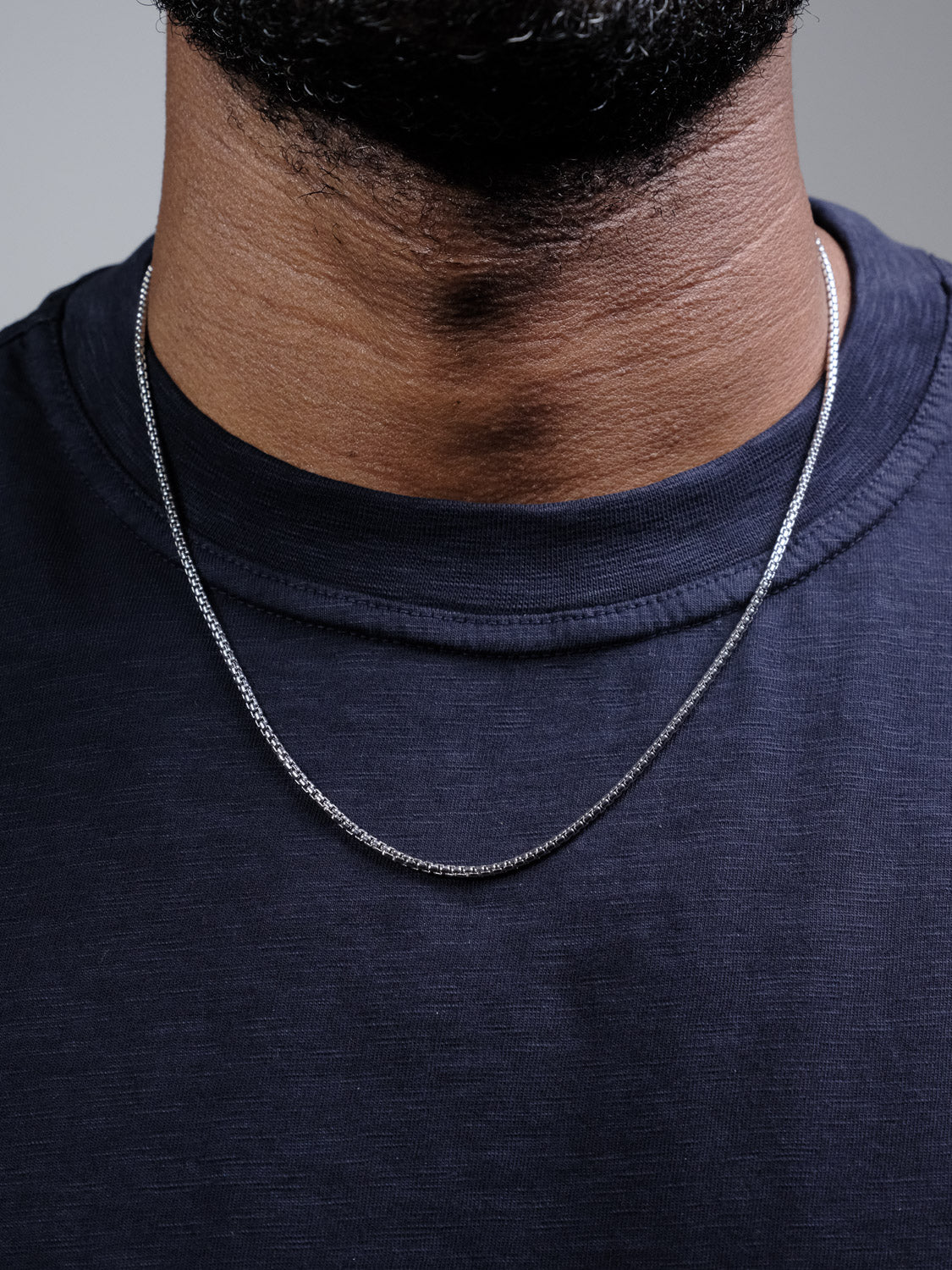 A close-up of a person wearing the Ezra 40 Box Chain Necklace by ID Menswear over a dark navy blue t-shirt, with their neck and lower face partially visible.