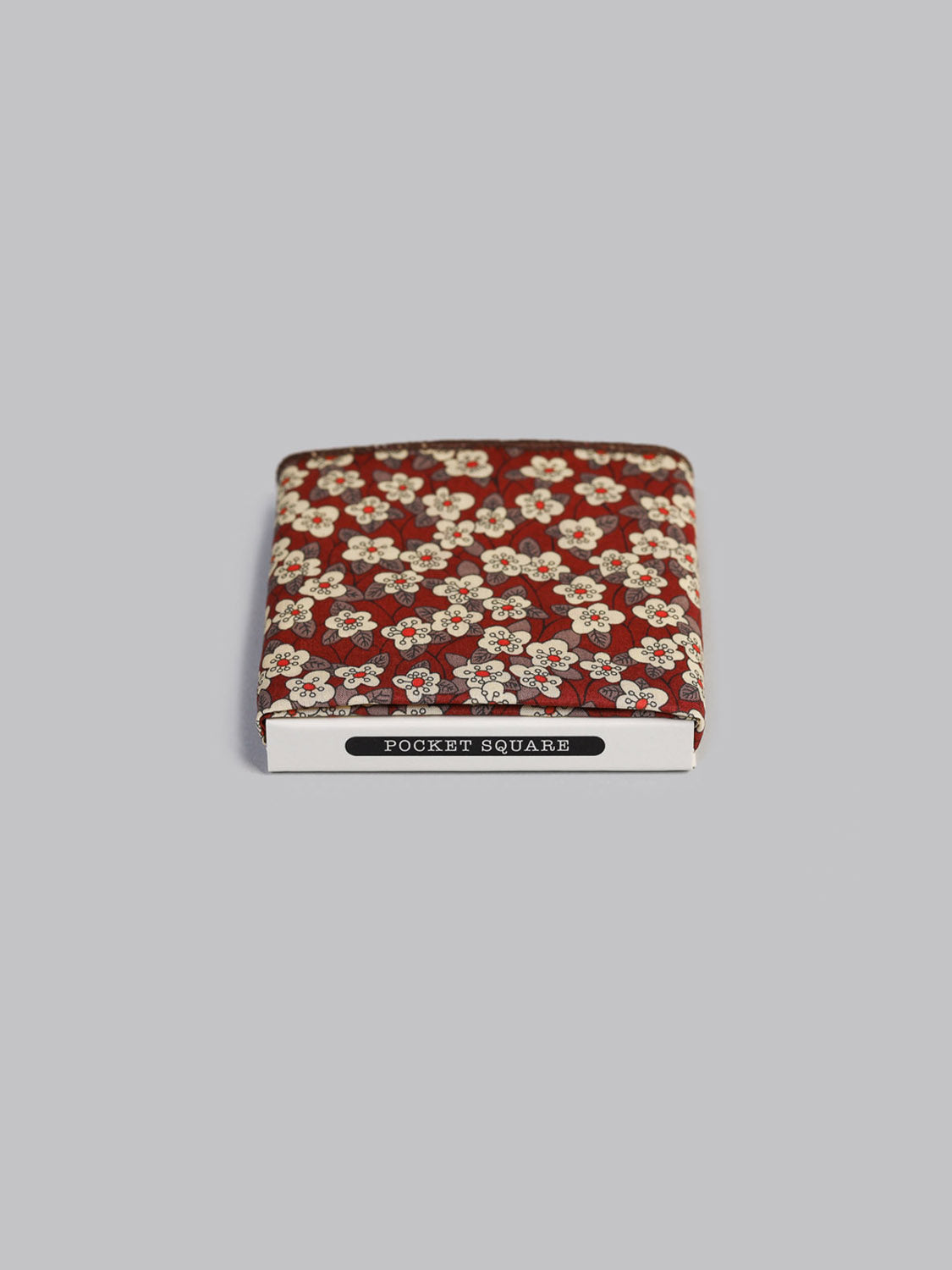 The Liberty™ Fion Pocket Square by ID Menswear, handmade in Brooklyn from red Tana Lawn cotton with a white floral print, is neatly boxed and displayed on a plain light gray background.