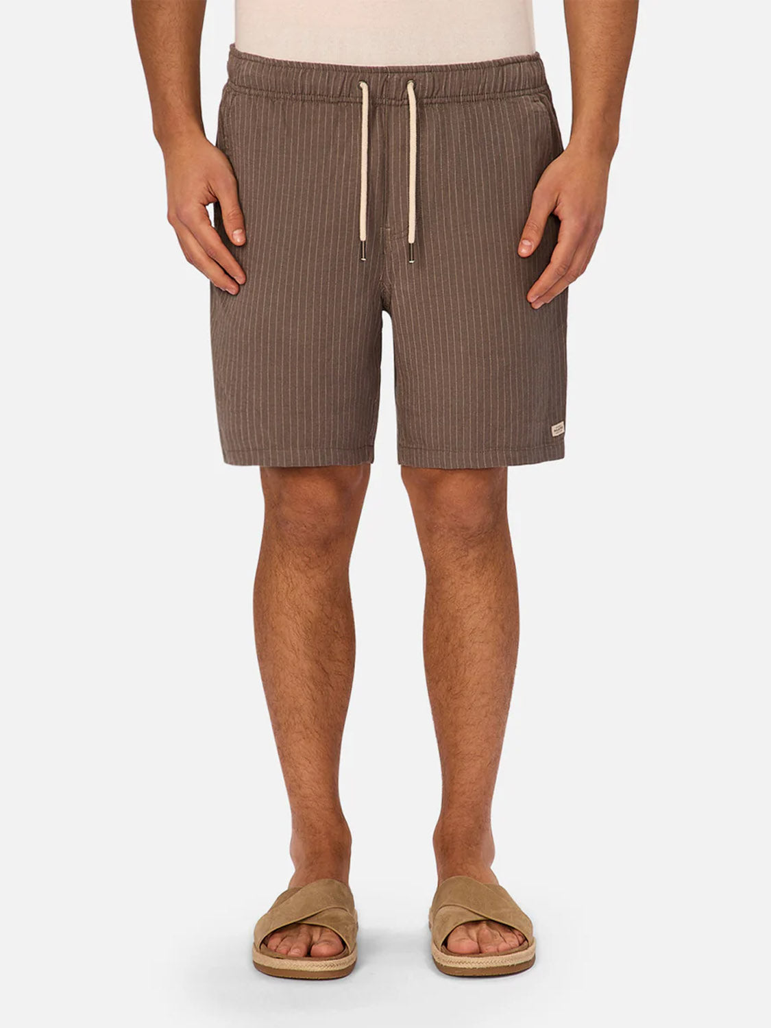 A person wearing Industrie’s The Fontera Short in brown pinstripes and beige slide sandals stands against a white background from the waist down. These shorts deliver breathable comfort and effortless style for warm days.