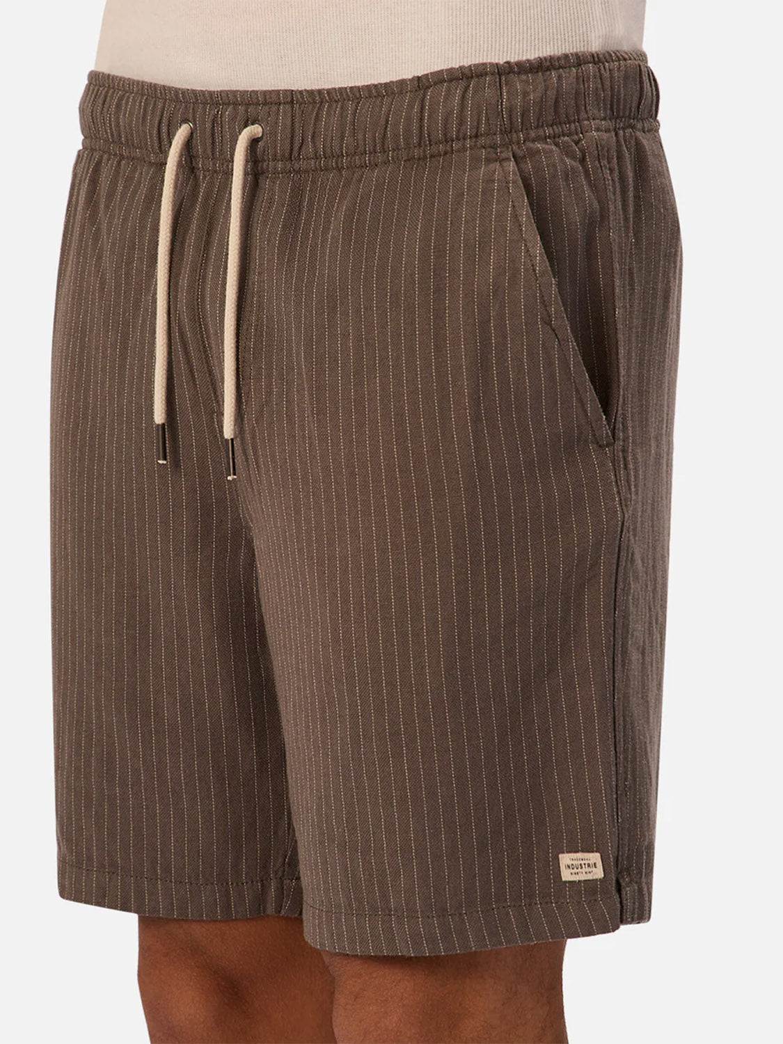 A person wearing The Fontera Short by Industrie—brown pinstripe shorts with a drawstring waist, side pockets, and a small rectangular label near the hem—ideal breathable shorts for warm days, shown from waist to mid-thigh.