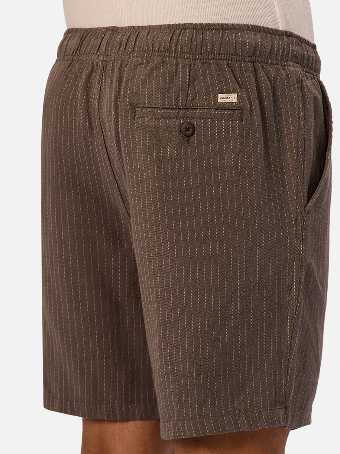 A close-up side view of a person wearing Industrie’s The Fontera Short, featuring breathable pinstripe fabric, an elastic waistband, a buttoned back pocket, and a small label above the pocket.