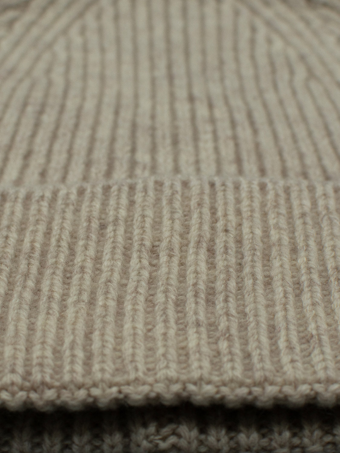 Close-up of a beige, ribbed knit fabric from the Fuji Merino Wool Beanie by ID Menswear. The texture and pattern of the 100% Merino Wool are prominently visible, showcasing its vertical lines—a perfect winter companion.