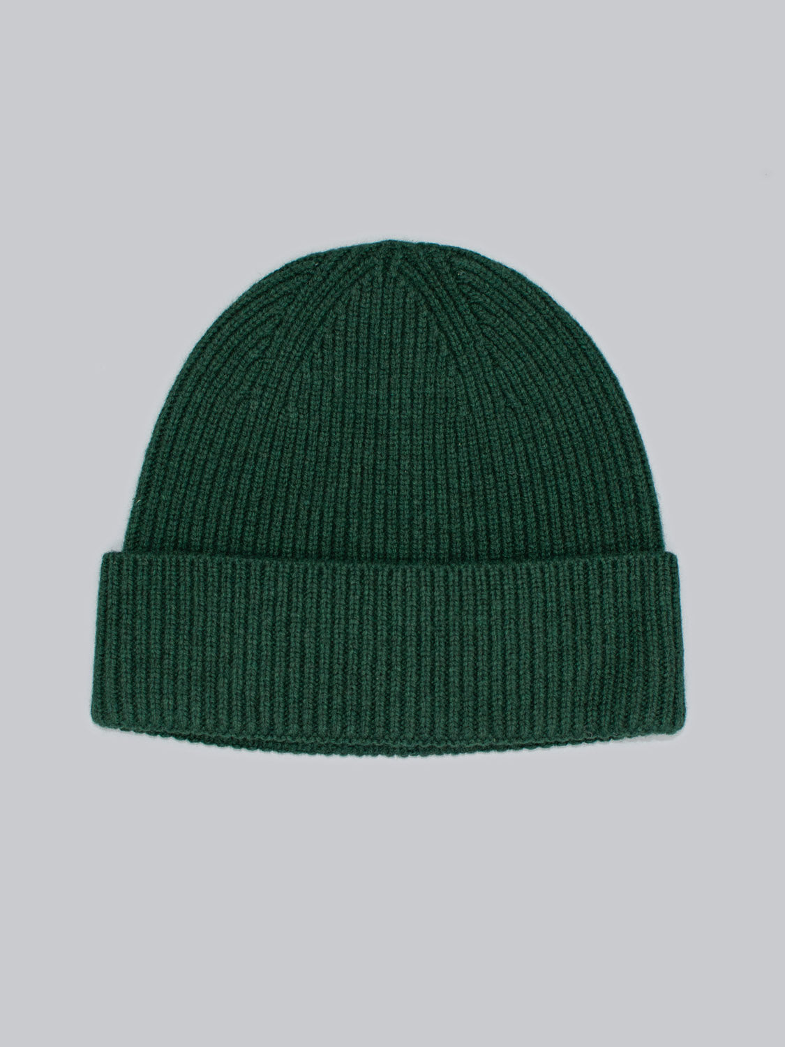 The Fuji Merino Wool Beanie from ID Menswear, featuring a dark green ribbed knit design and folded cuff made of warm Merino wool, rests on a gray background. Its texture highlights a simple and stylish look ideal for chilly days.