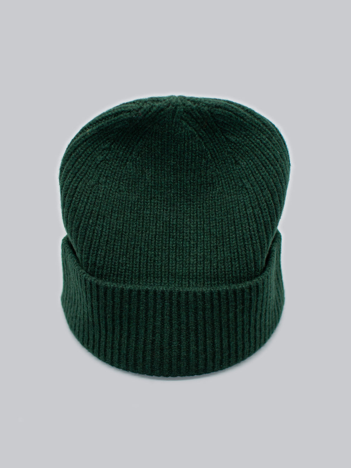 The Fuji Merino Wool Beanie by ID Menswear is a dark green ribbed knit hat with a folded cuff, made of warm merino wool, showcased against a plain gray background.