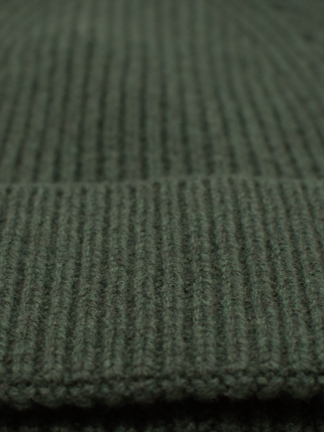 The Fuji Merino Wool Beanie from ID Menswear features a close-up of green, ribbed knit fabric with vertical lines and a folded edge, highlighting its cozy warmth—ideal for winter wear.