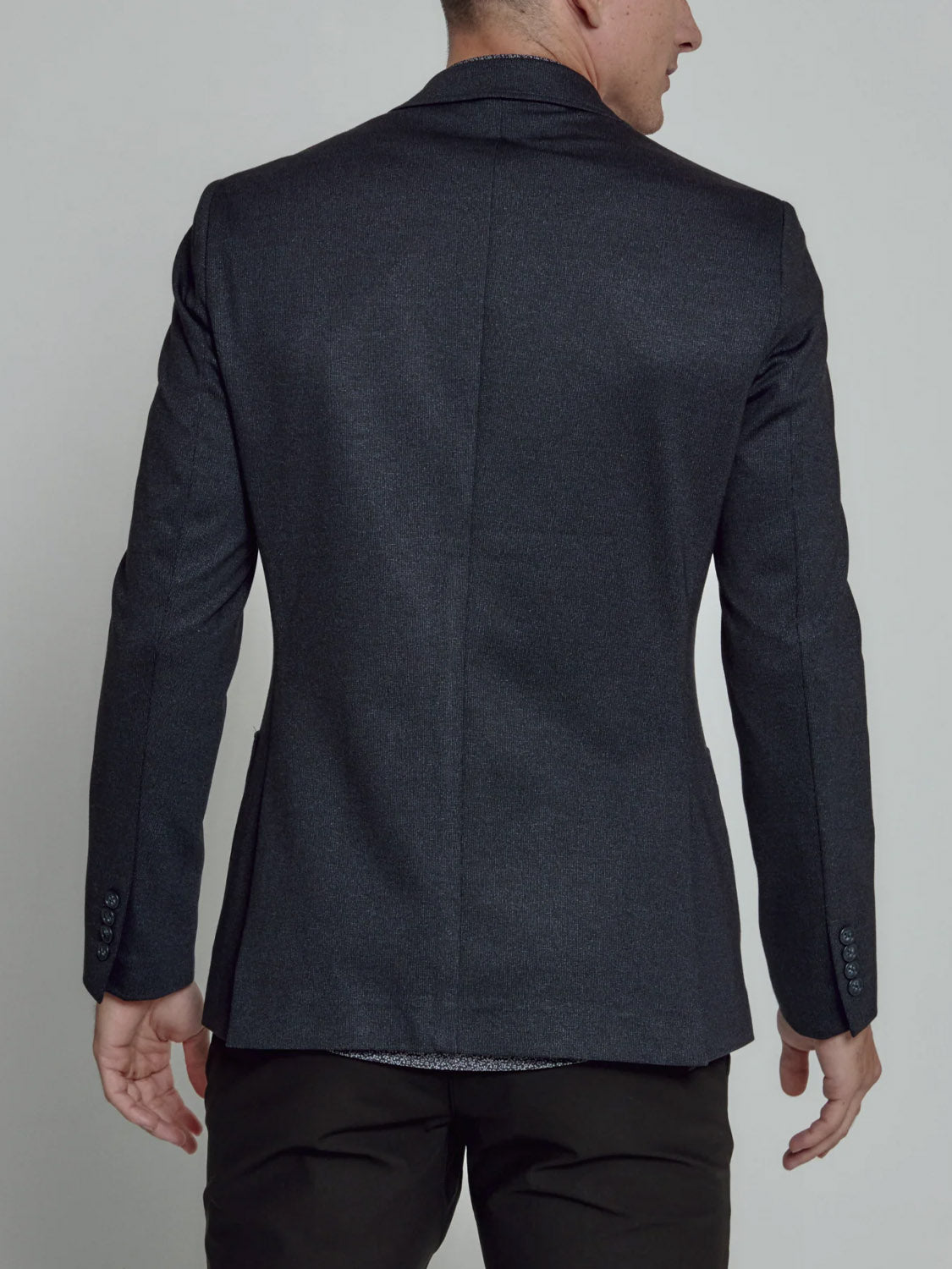 A man is seen from the back wearing the 7 Diamonds Gatsby Blazer in dark grey with a notched lapel, paired with black pants against a plain light background.