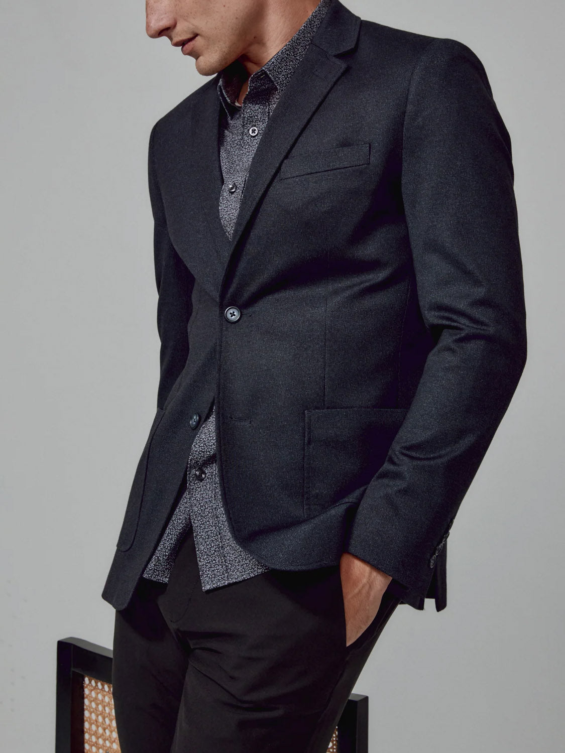 A man wearing the 7 Diamonds Gatsby Blazer over a patterned button-up shirt stands with one hand in his pocket, looking down against a plain background.