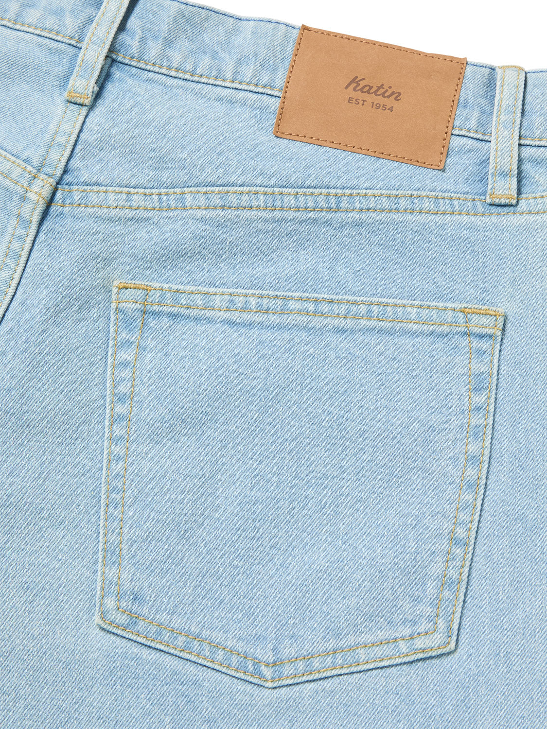 Close-up of the back pocket and waistband of the relaxed-fit Katin George 64 Short - 20 in light blue. A brown leather patch with Katin EST 1954 is stitched onto the waistband. The shorts, with their classic wash, feature yellow stitching.