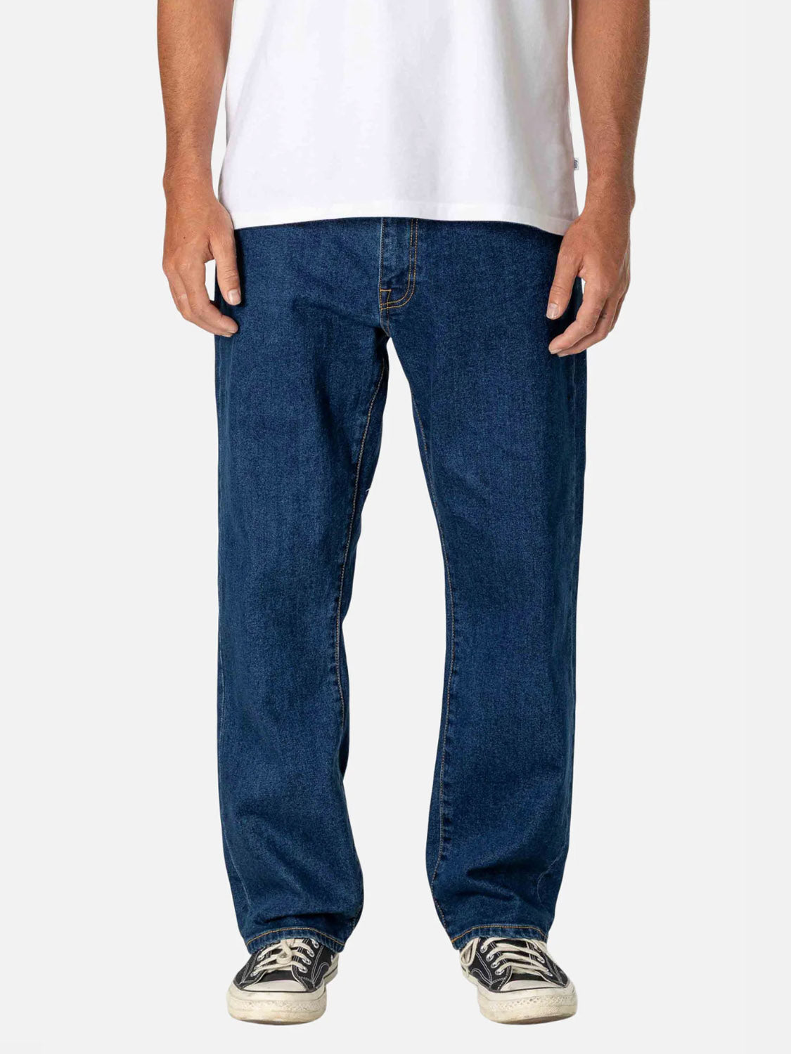 A person wearing George 64 Relaxed Pants by Katin in dark blue, a plain white T-shirt, and black-and-white sneakers stands against a plain light background. The person's face is not visible.