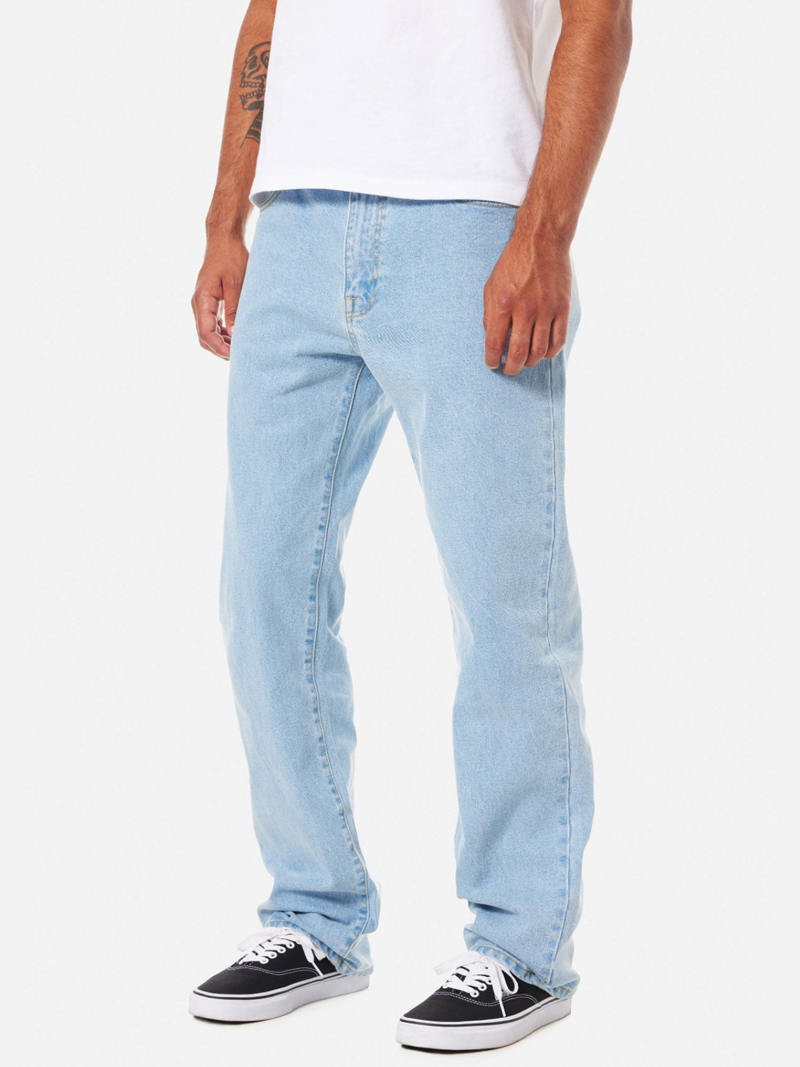 A man, visible from the waist down, wears Katin's George 64 Relaxed Pants in light blue paired with a white t-shirt and black-and-white sneakers, standing against a plain white background.