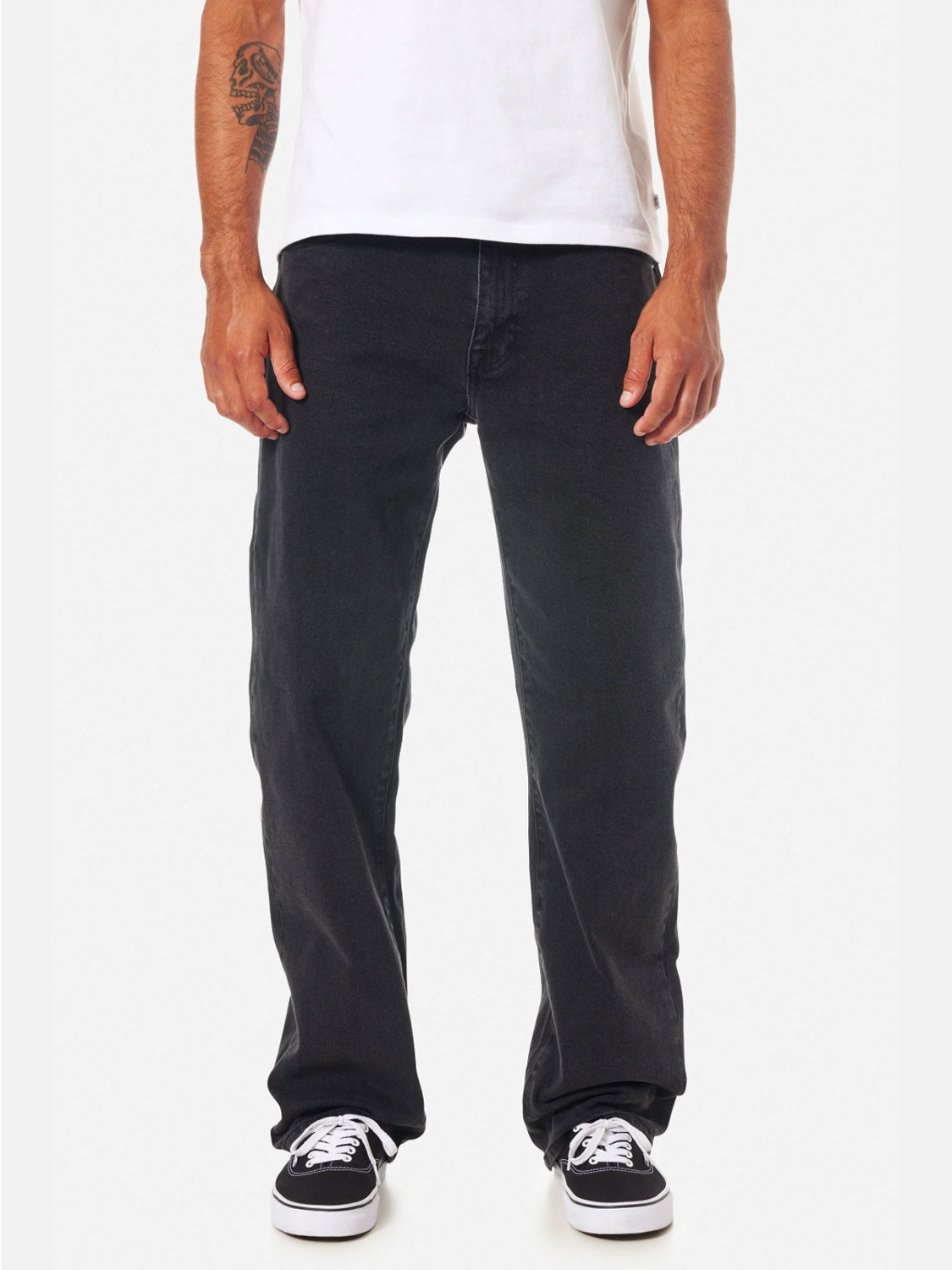 Man wearing a white t-shirt, Katin George 64 Relaxed Pants in black with a classic 5-pocket design, and black-and-white sneakers, standing with arms relaxed at his sides; tattoo visible on left arm.