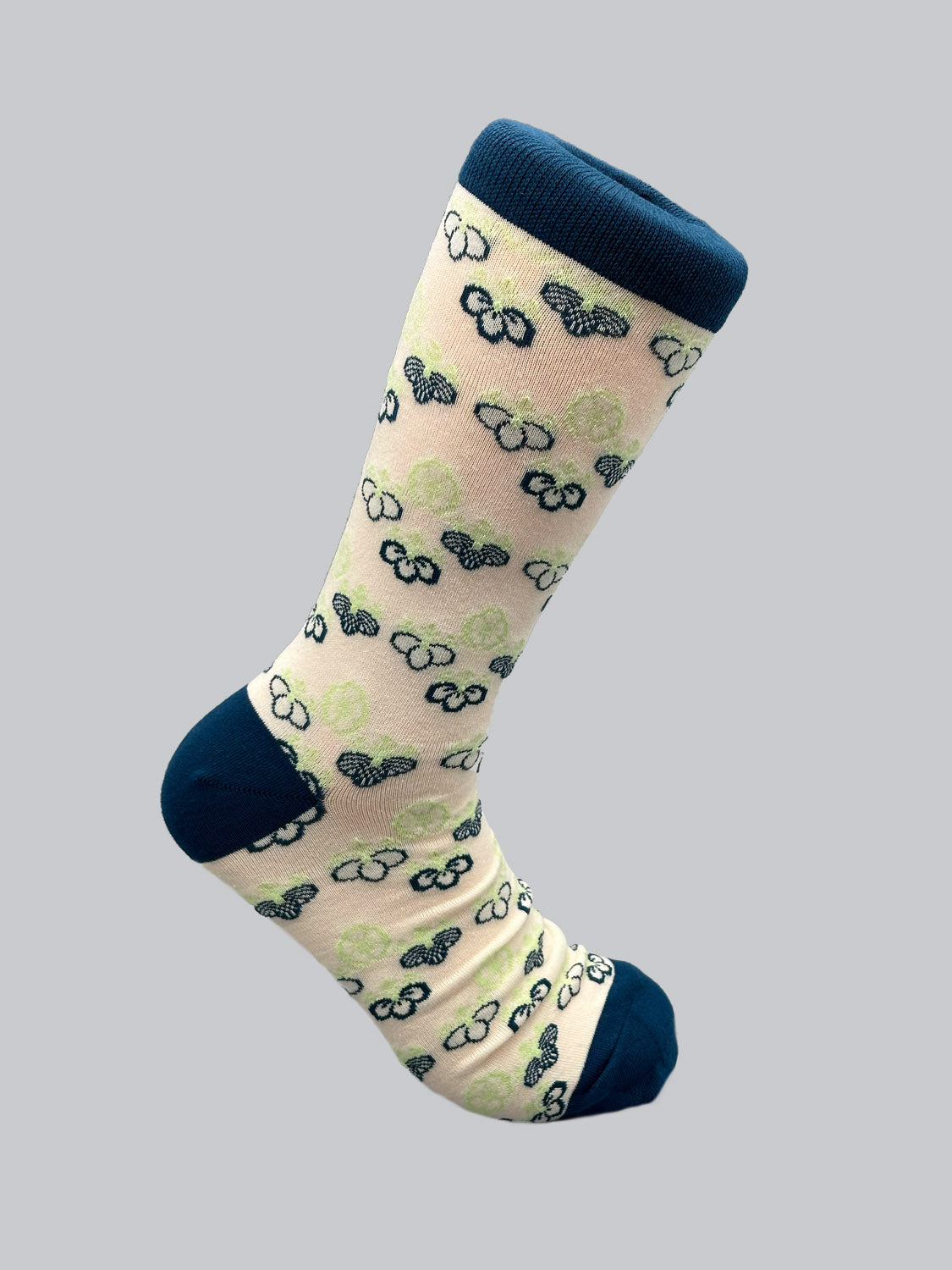 The Giri Graphic Sock by ID Menswear is a beige sock adorned with stylish Japanese patterns of green and navy clouds, complemented by a navy heel, toe, and cuff. It boasts a soft, luxurious feel and is elegantly displayed against a light grey background.