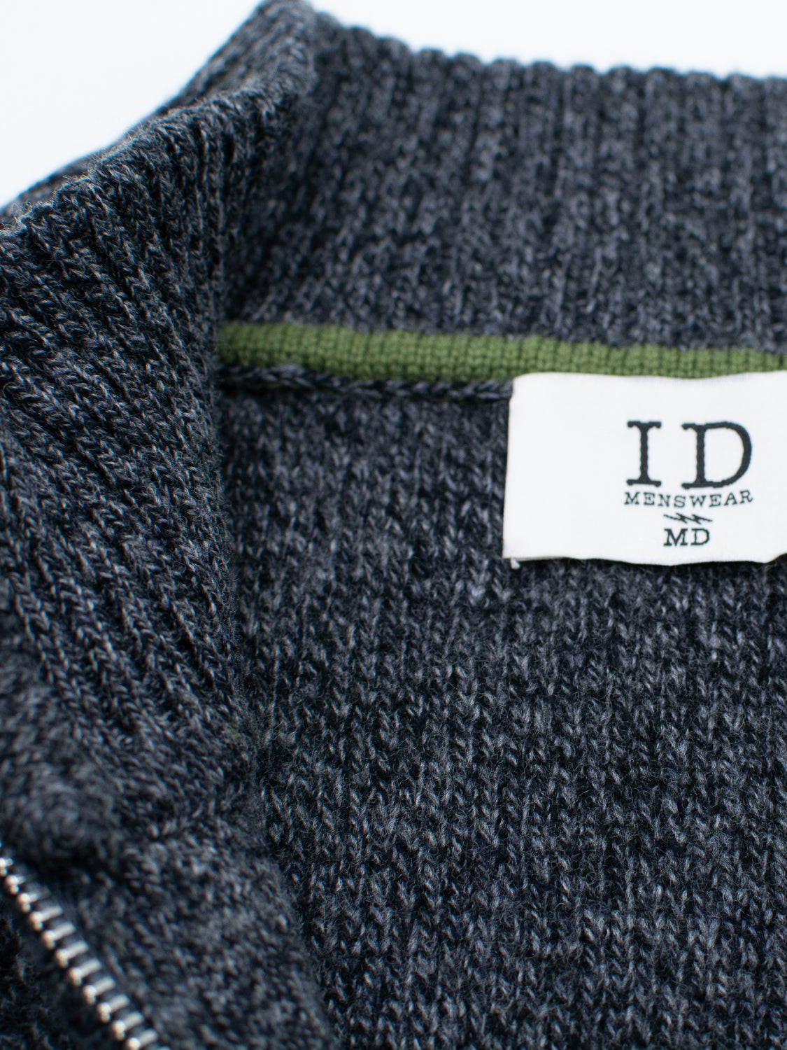Close-up of the Glasgow Zip Up Sweater by ID Menswear, featuring a dark gray merino wool fabric, a visible collar with a white "ID Menswear" label, and a thin green strip lining the lightweight sweater’s collar.