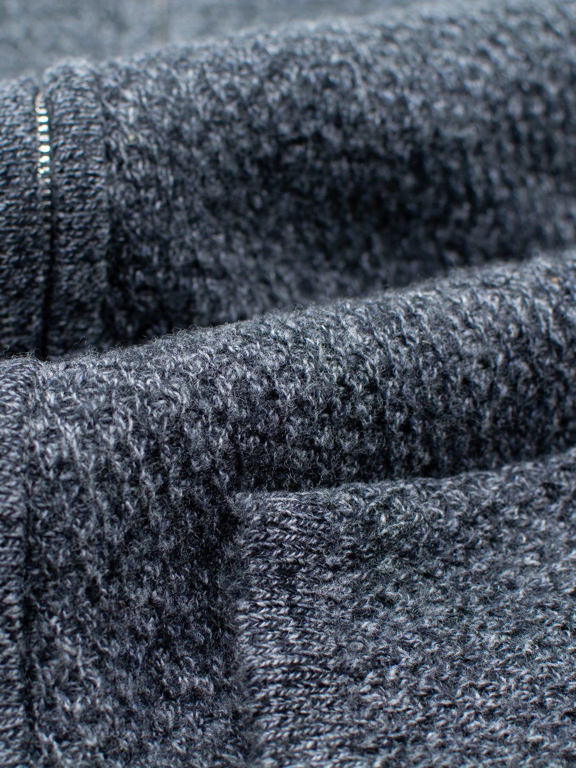 Close-up of the Glasgow Zip Up Sweater by ID Menswear shows the dark gray merino wool knit fabric, highlighting its soft, textured surface and detailed weave.