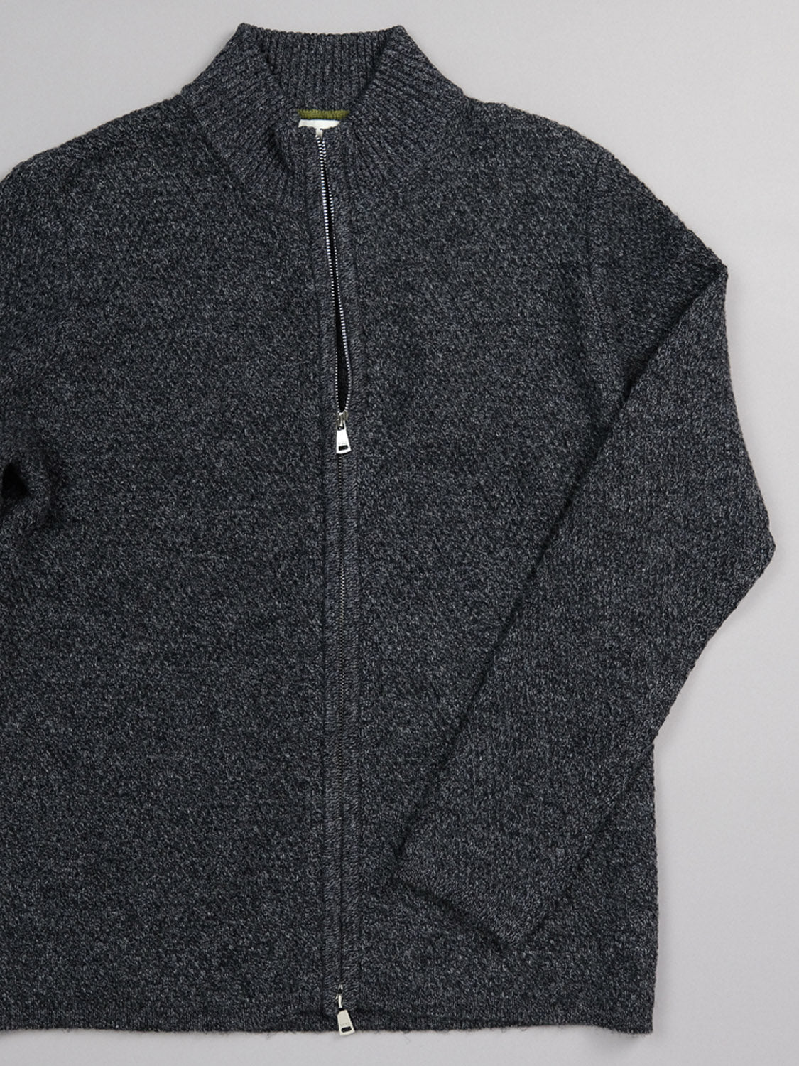 The Glasgow Zip Up Sweater by ID Menswear, in dark gray merino wool with a textured knit, long sleeves, and a stand-up collar, is shown laid flat on a light gray surface.
