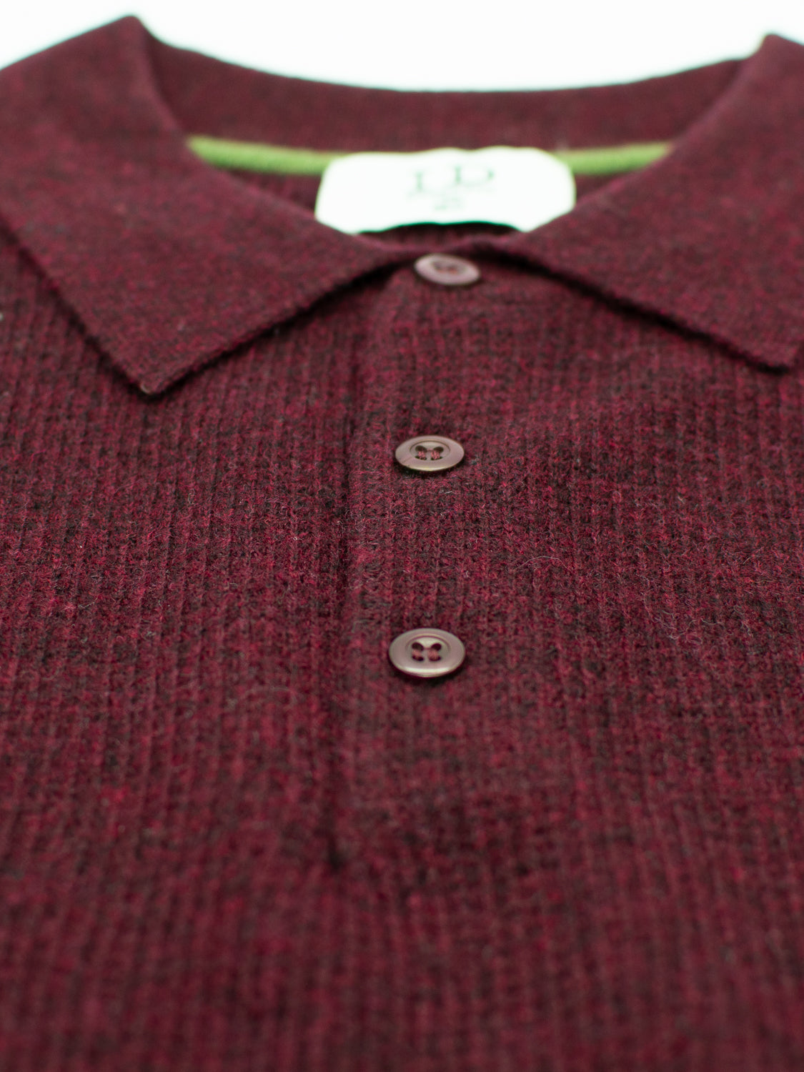 Close-up of a Gothenberg Merino Sweater Polo by ID Menswear in maroon, featuring a textured grid pattern. Its a long-sleeve polo with a collar and three buttons in the front, showcasing casual elegance with an inside collar tag visible.