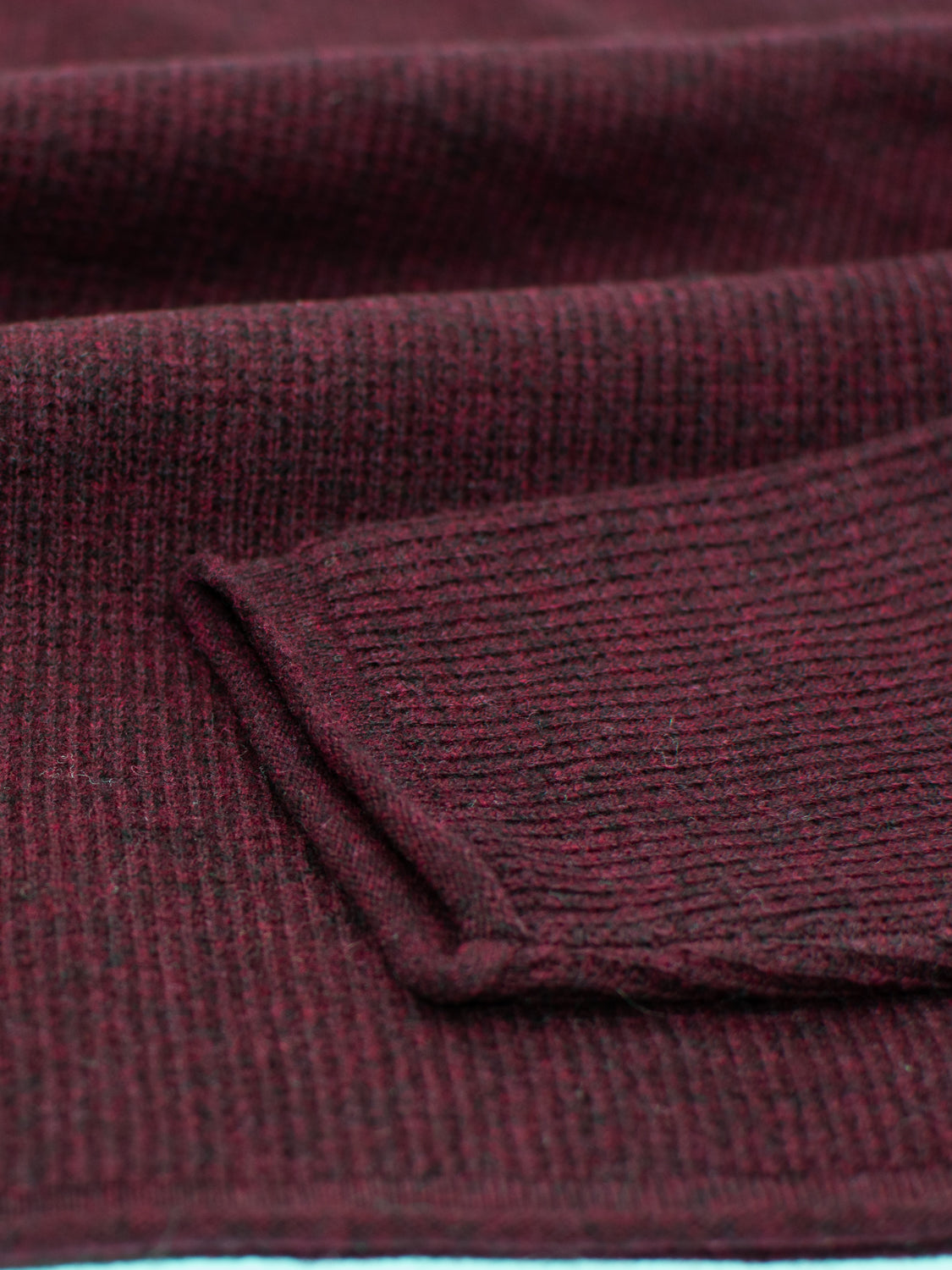 Close-up of folded maroon knitted fabric with a ribbed texture, exuding soft, warm vibes. Made from premium fabric by ID Menswear, the Gothenberg Merino Sweater Polo combines casual elegance and cozy comfort, perfect as a sweater or scarf.