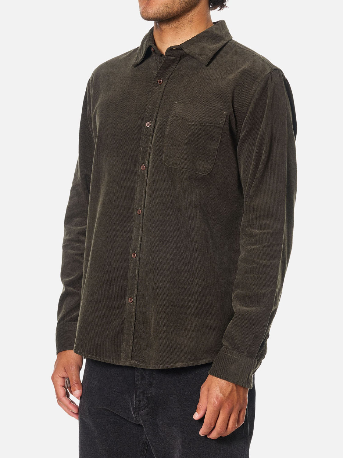 A person wears the Katin Granada Shirt, a long-sleeve dark olive green cotton corduroy button-down with a chest pocket, paired with black pants, standing against a white background. The person's head is partially out of the frame.