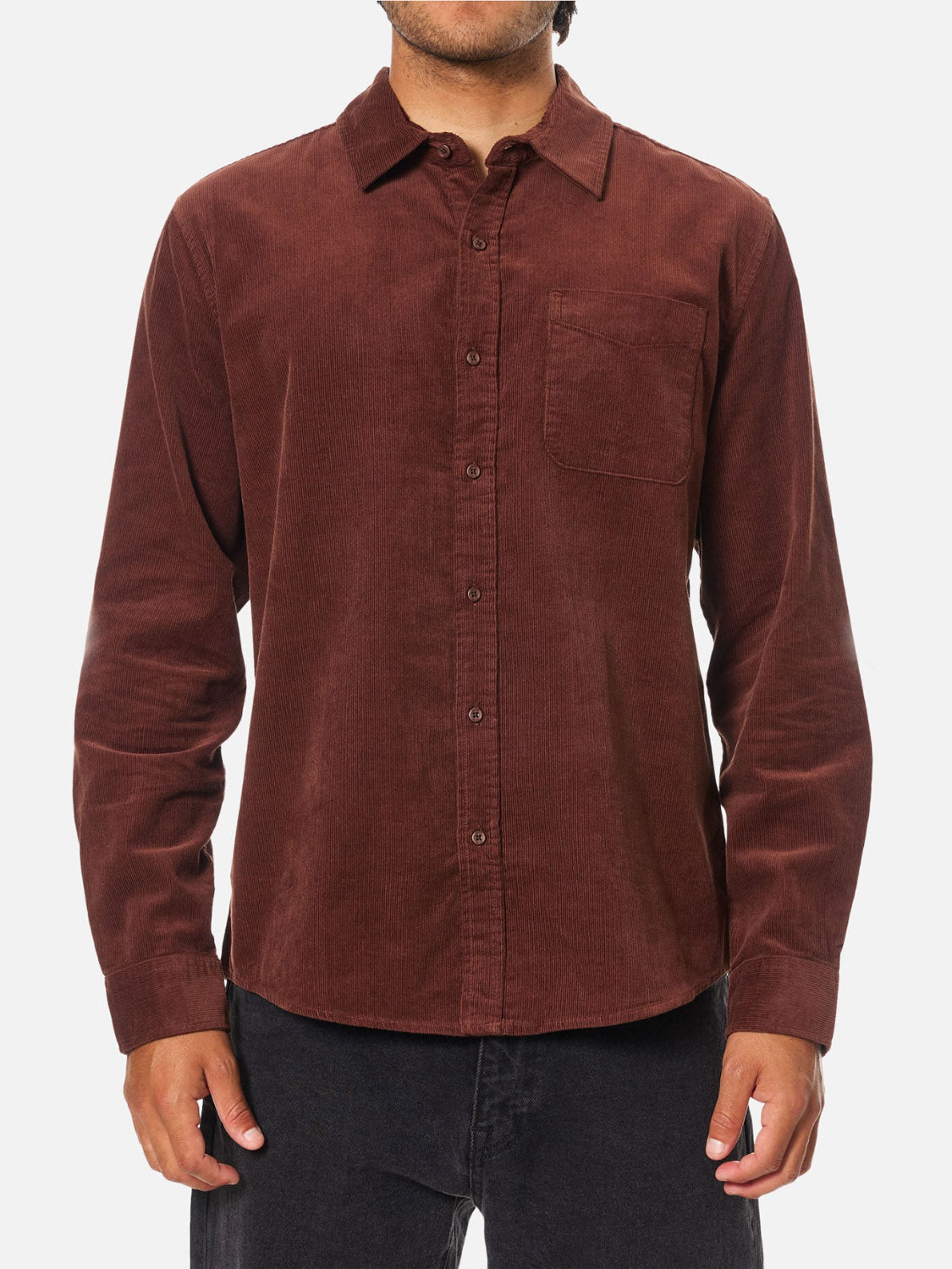 A man wearing the Katin Granada Shirt—a brown, long-sleeve, button-down corduroy shirt with a front pocket—paired with dark pants, stands against a plain white background.